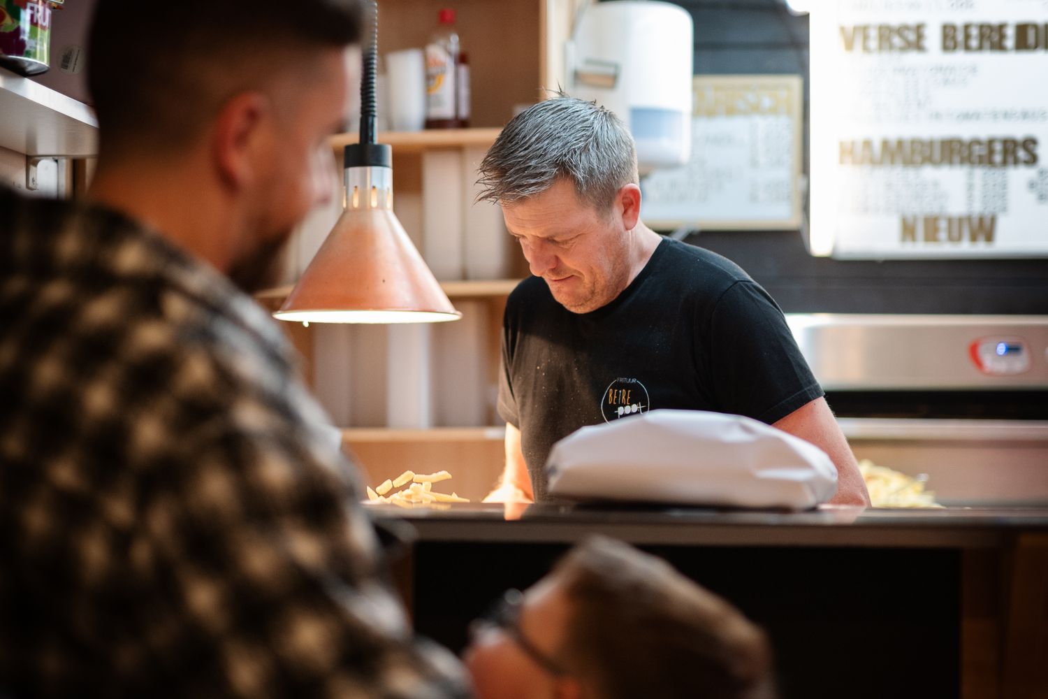 Chef preparing fresh burgers at a restaurant kitchen counter under warm pendant lighting.