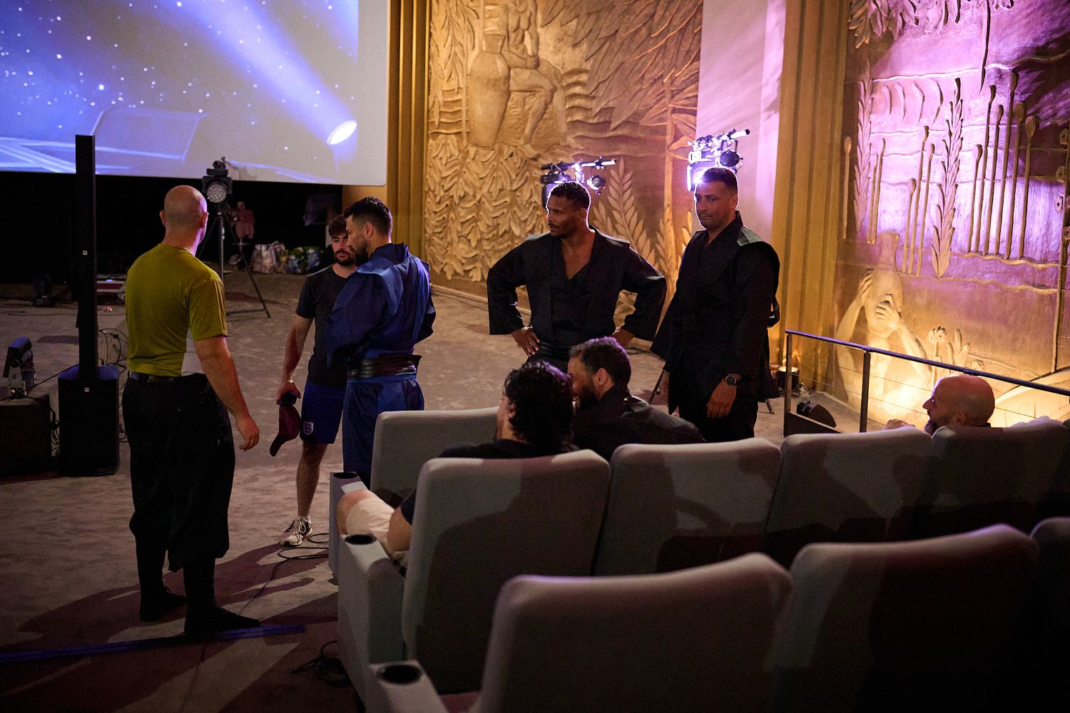 Group of people in costumes gathered in a dramatic Egyptian-themed room with ornate wall carvings and colorful lighting.