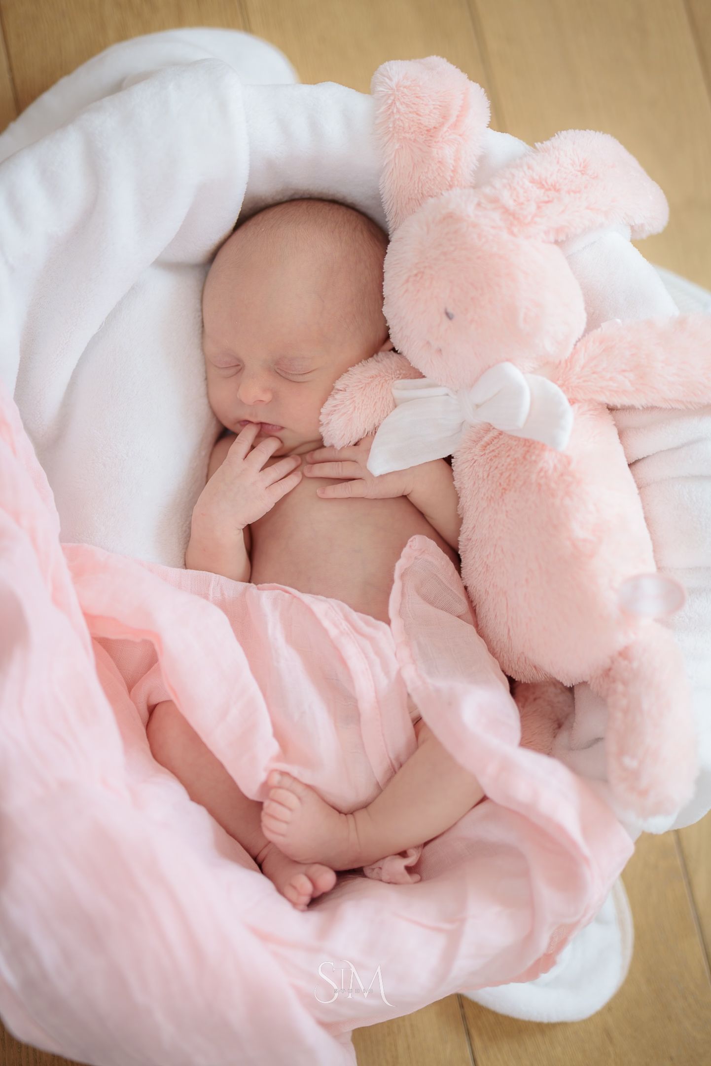 Peaceful newborn baby sleeping in white basket with pink bunny stuffed animal and blanket.