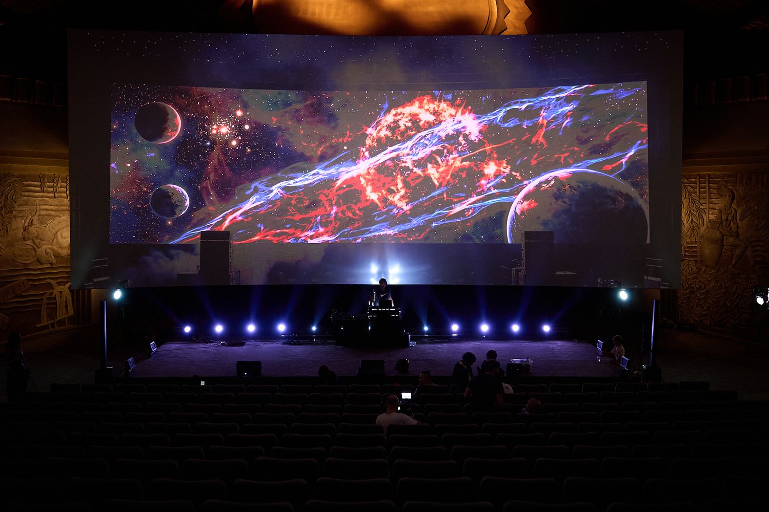 A stunning cosmic nebula display on a large theater screen with colorful space imagery and dramatic stage lighting.