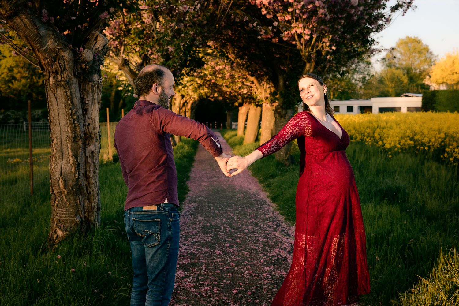 Couple in red outfits holding hands on a flower-lined path at golden hour in a lush green garden.