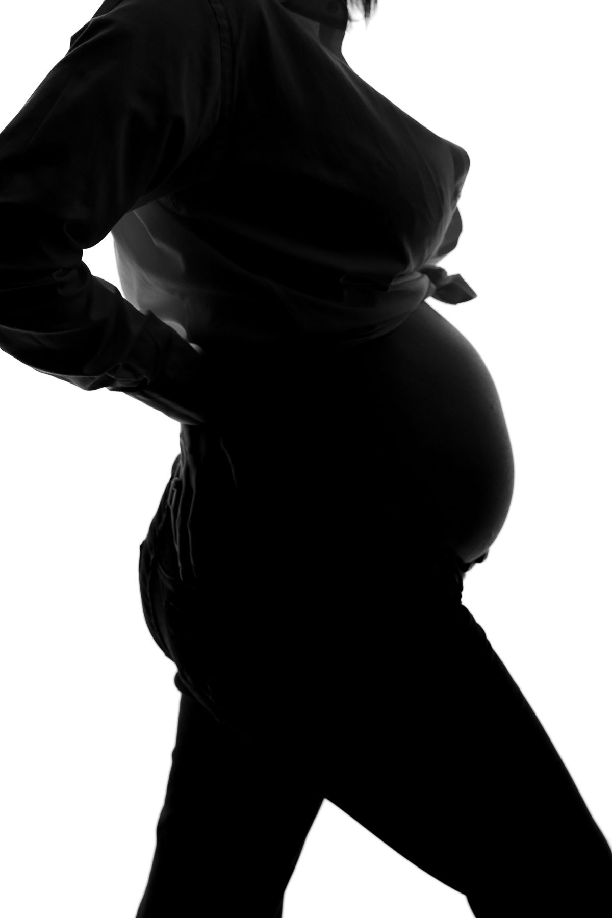 Black and white silhouette of a pregnant woman standing sideways, showcasing her baby bump against white background.