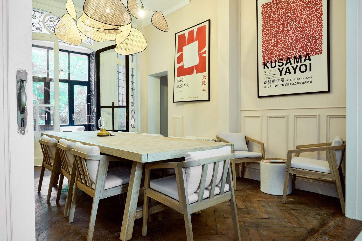 Elegant dining room with herringbone floors, white wainscoting, Kusama Yayoi art print, and modern wooden chairs around a marble table.