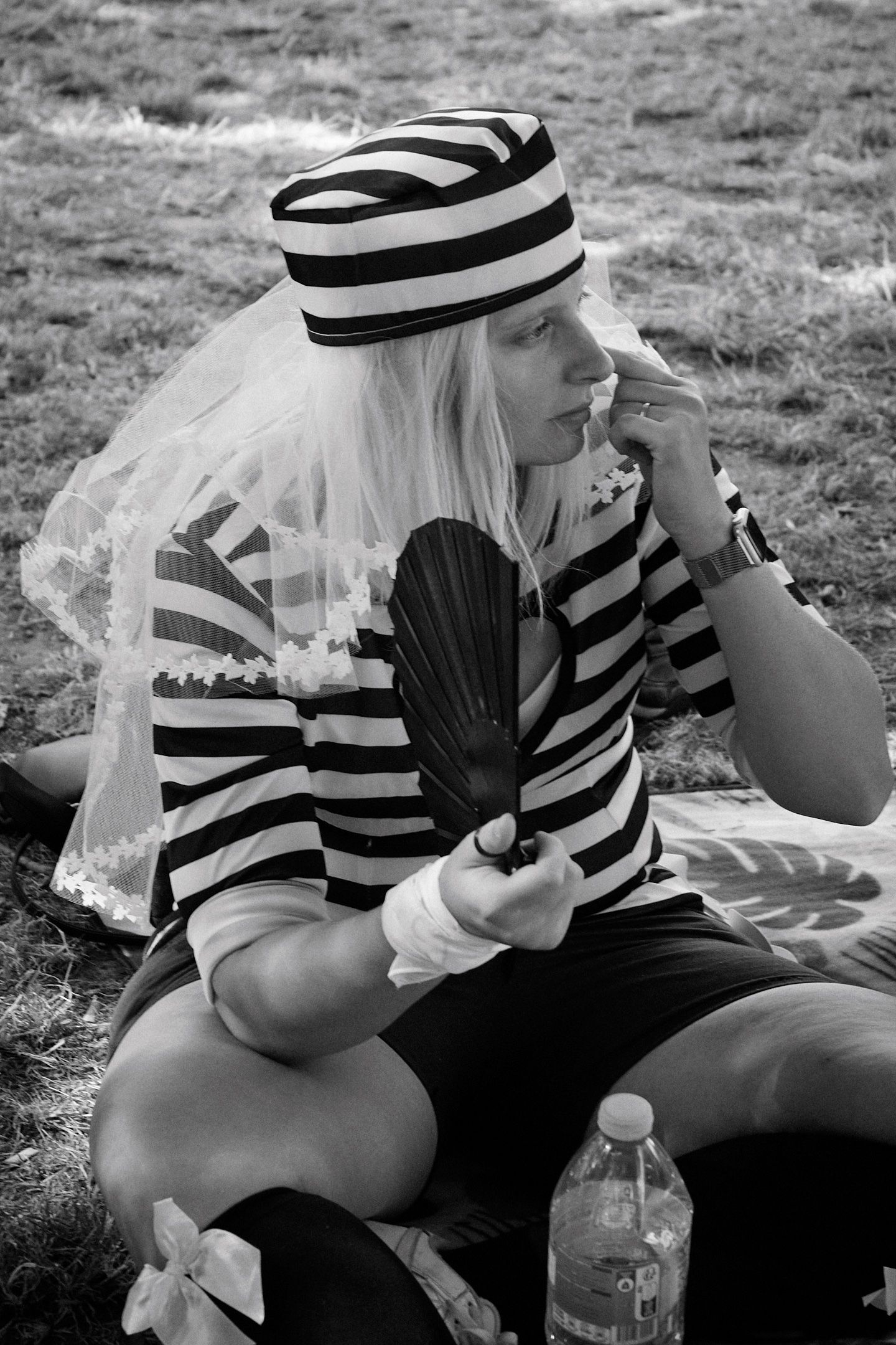 Black and white photo of a woman in striped costume with veil hat holding a fan outdoors.