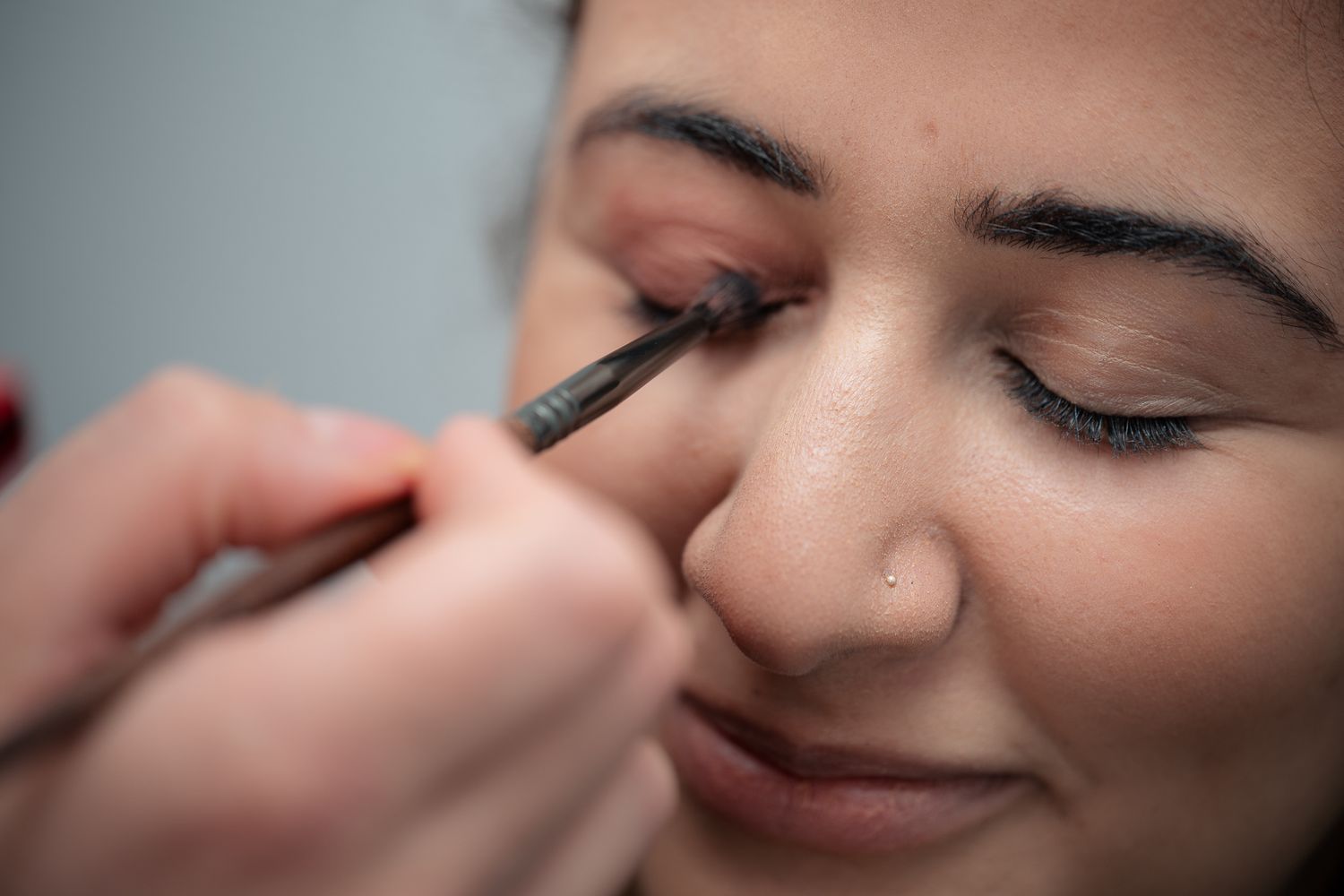 Close-up of a makeup artist applying eyeliner to a young woman's eye with a precision brush.