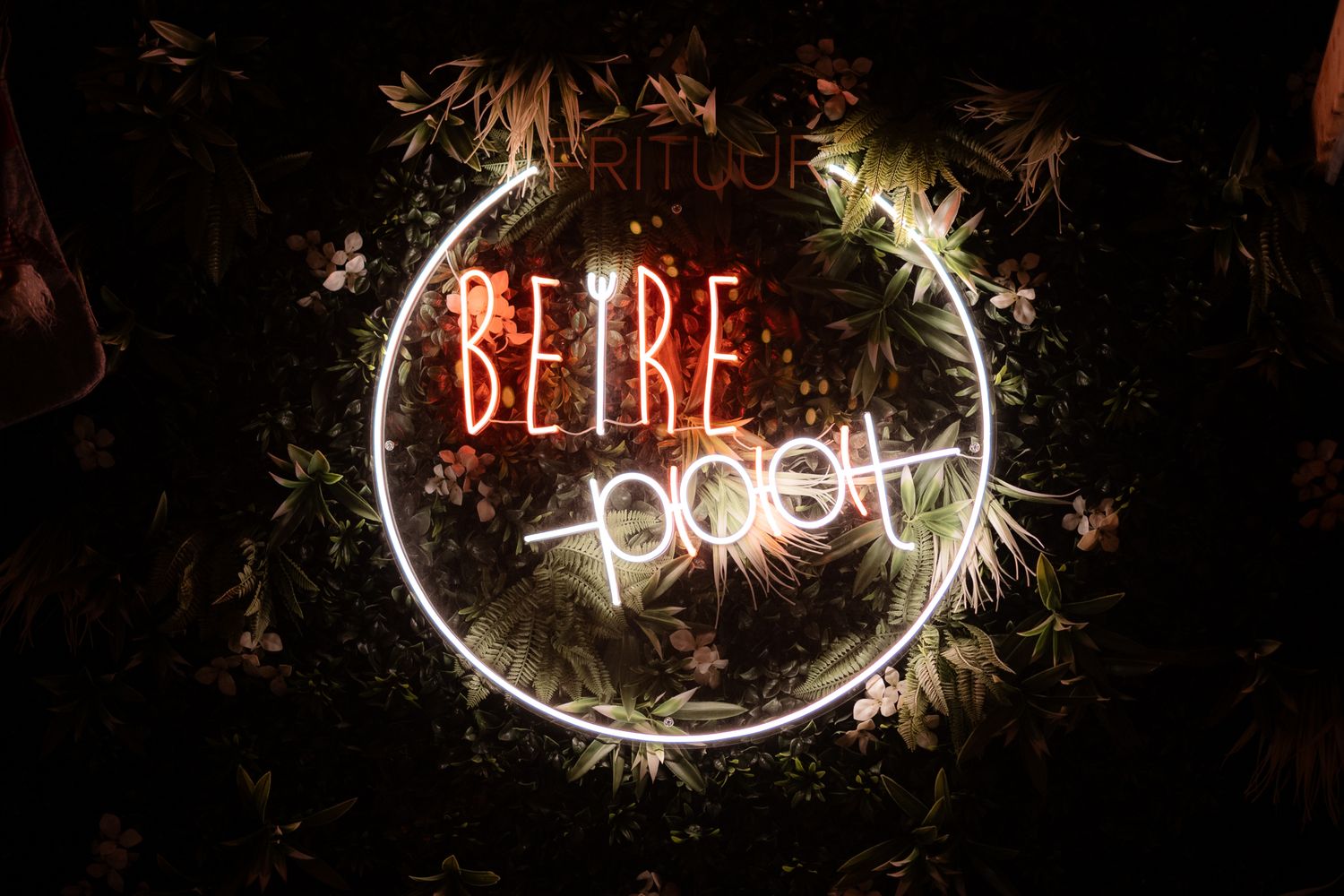 Glowing neon sign reading 'BEIRE pool' surrounded by a circular light frame and tropical greenery in dark setting.