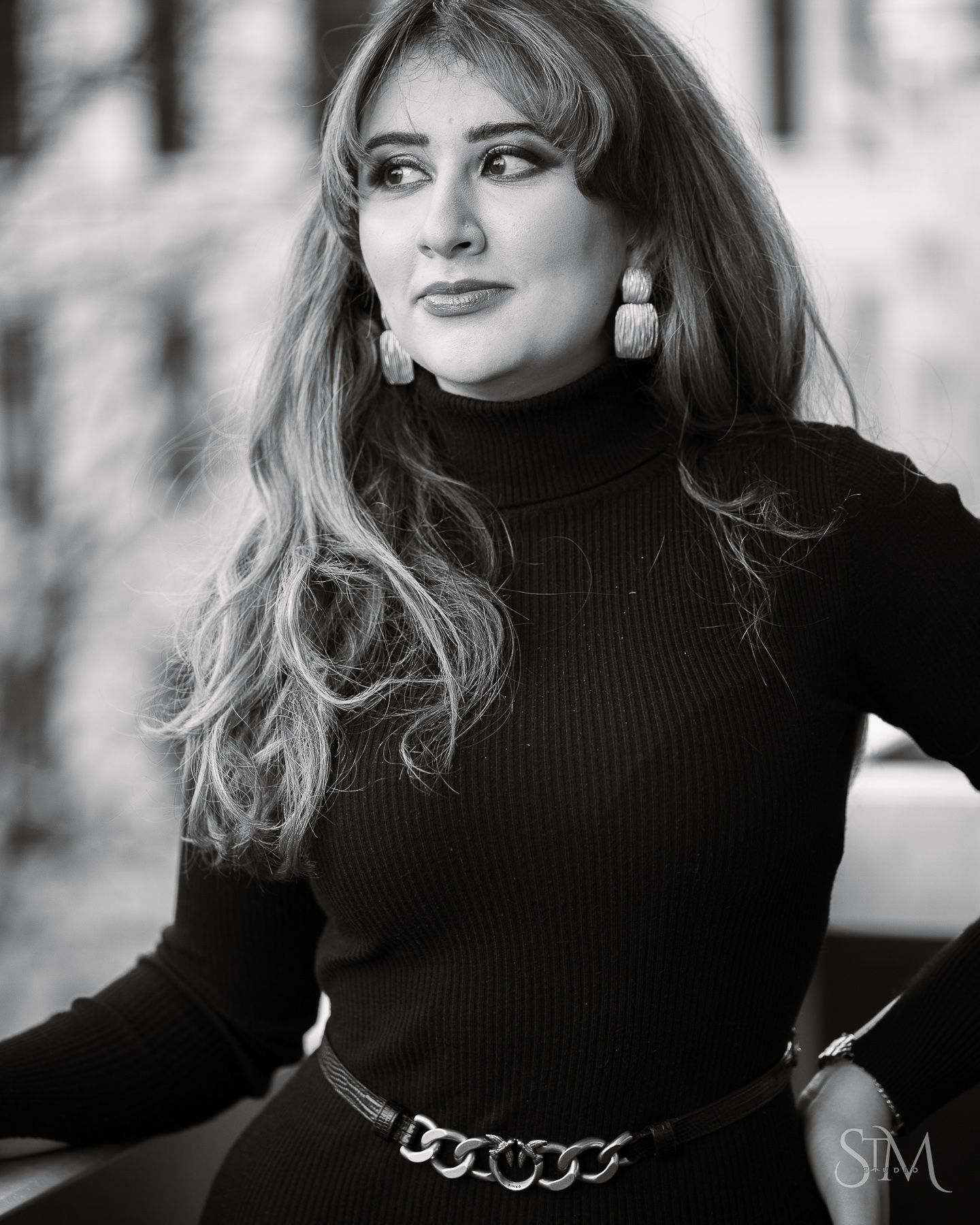 Black and white portrait of a stylish woman in a turtleneck with chain belt outdoors.