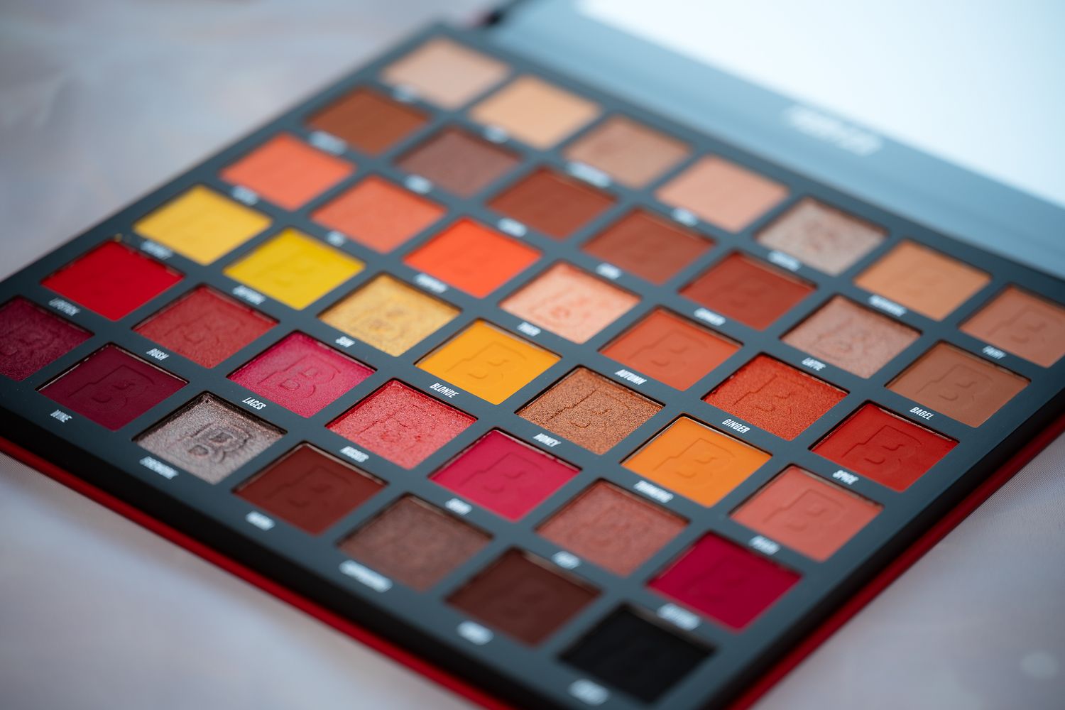 Close-up of a vibrant eyeshadow palette featuring warm red, orange, and yellow shades arranged in neat rows.