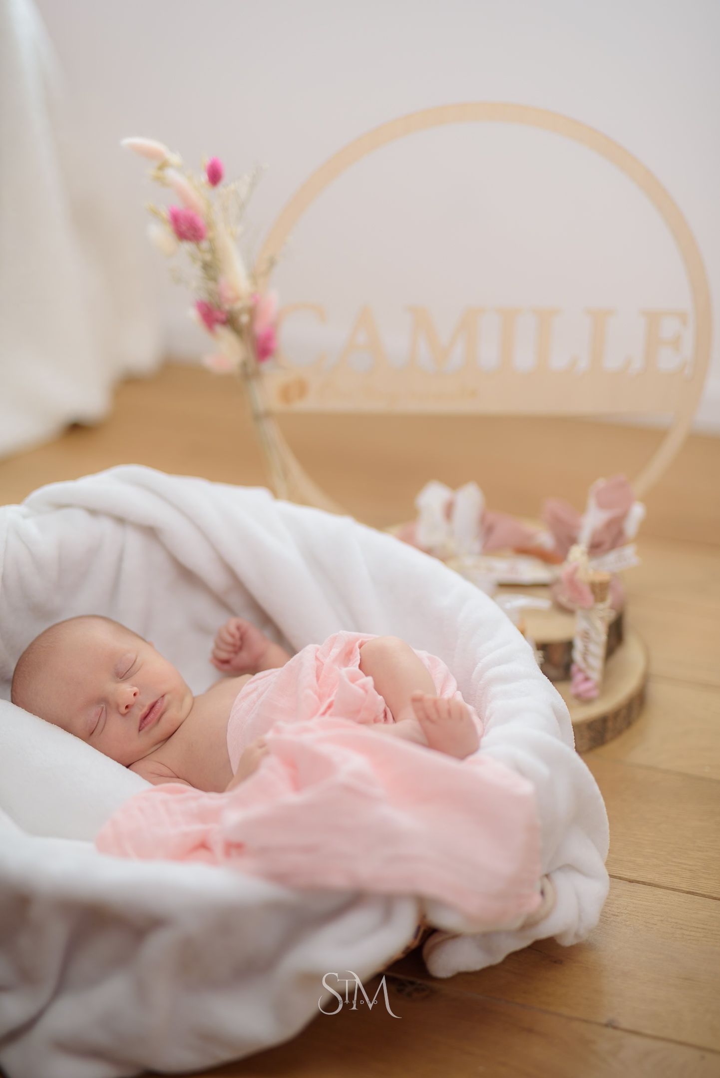 Sleeping newborn baby girl named Camille wrapped in pink, resting in a white Moses basket.