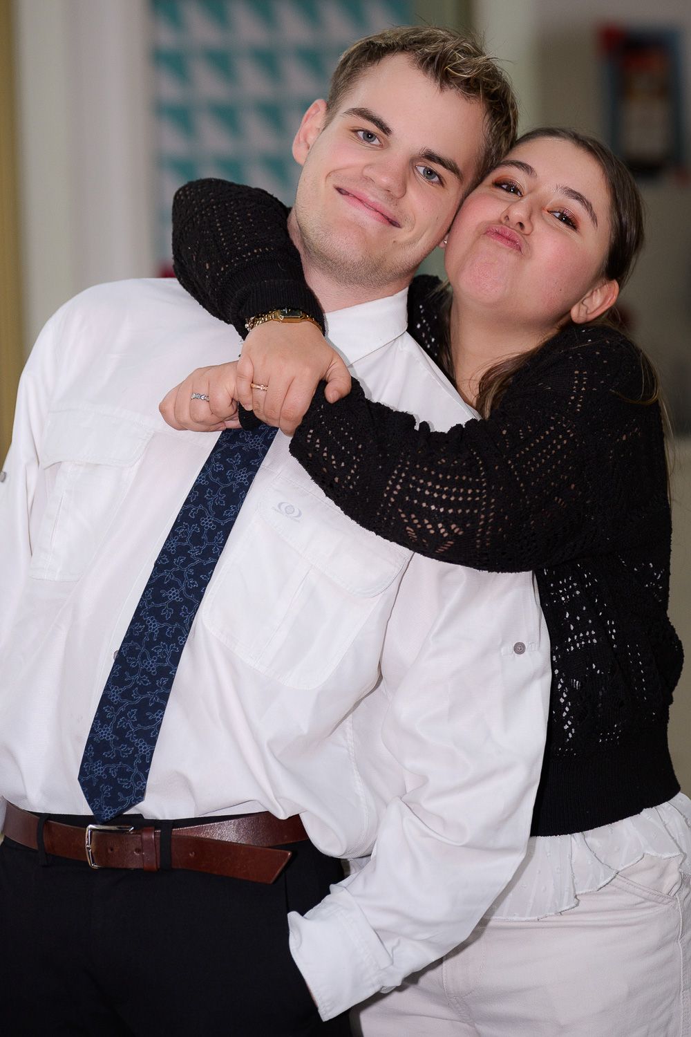 Young couple posing playfully, woman hugging man from behind while he smiles at the camera.