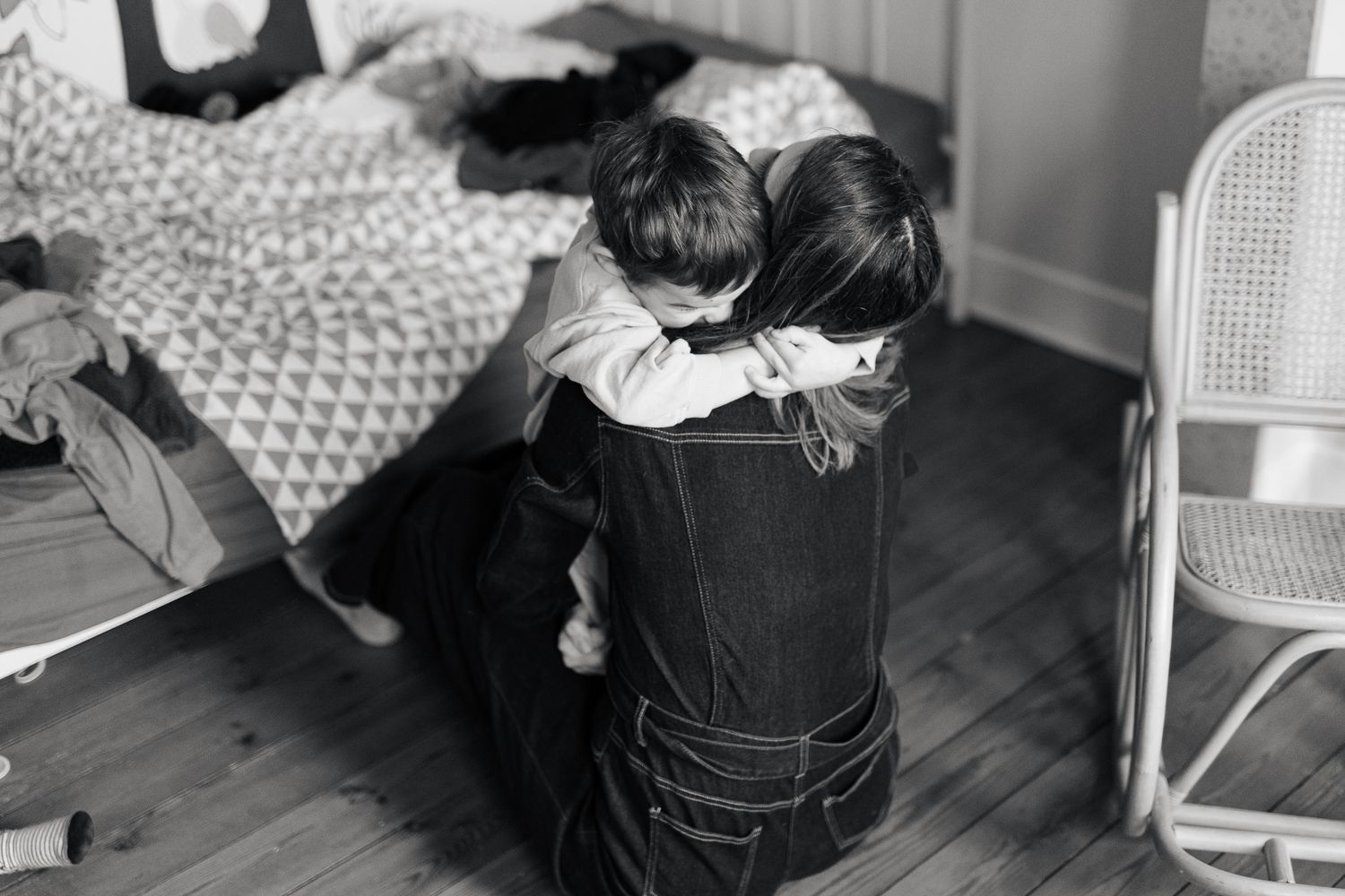 Young child embracing a kneeling parent in a warm hug in a black and white home photo.