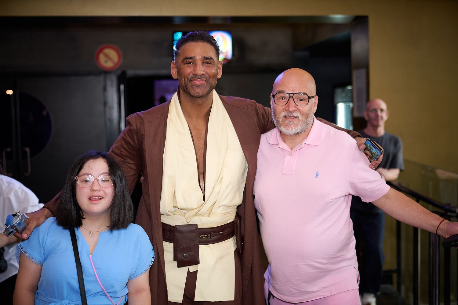 Man in Jedi costume poses with two people at a Star Wars themed event.