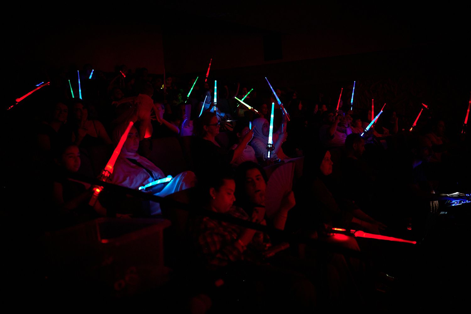 Audience members wave colorful LED light sticks in a dark concert venue.