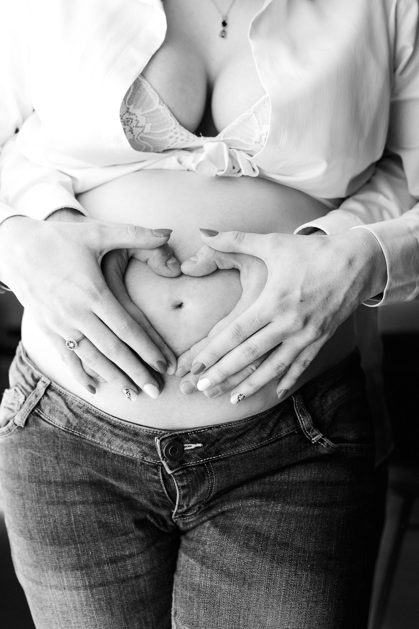 Black and white photo of pregnant woman with partner forming heart shape with hands on baby bump.