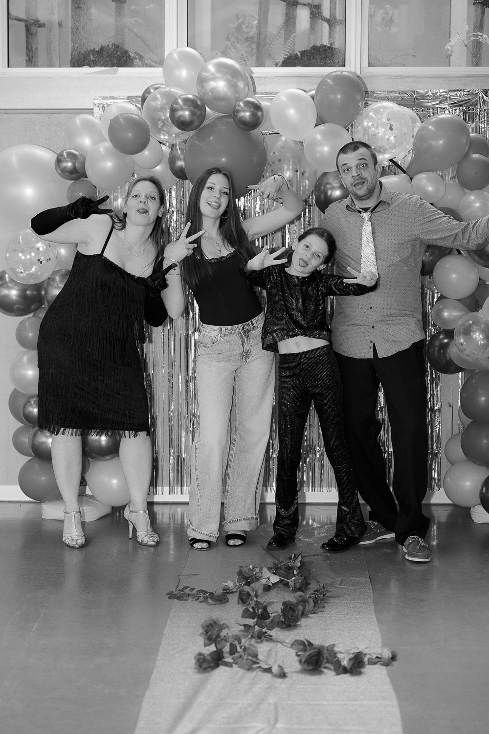 Four people posing together in front of a balloon arch backdrop at a celebration event.