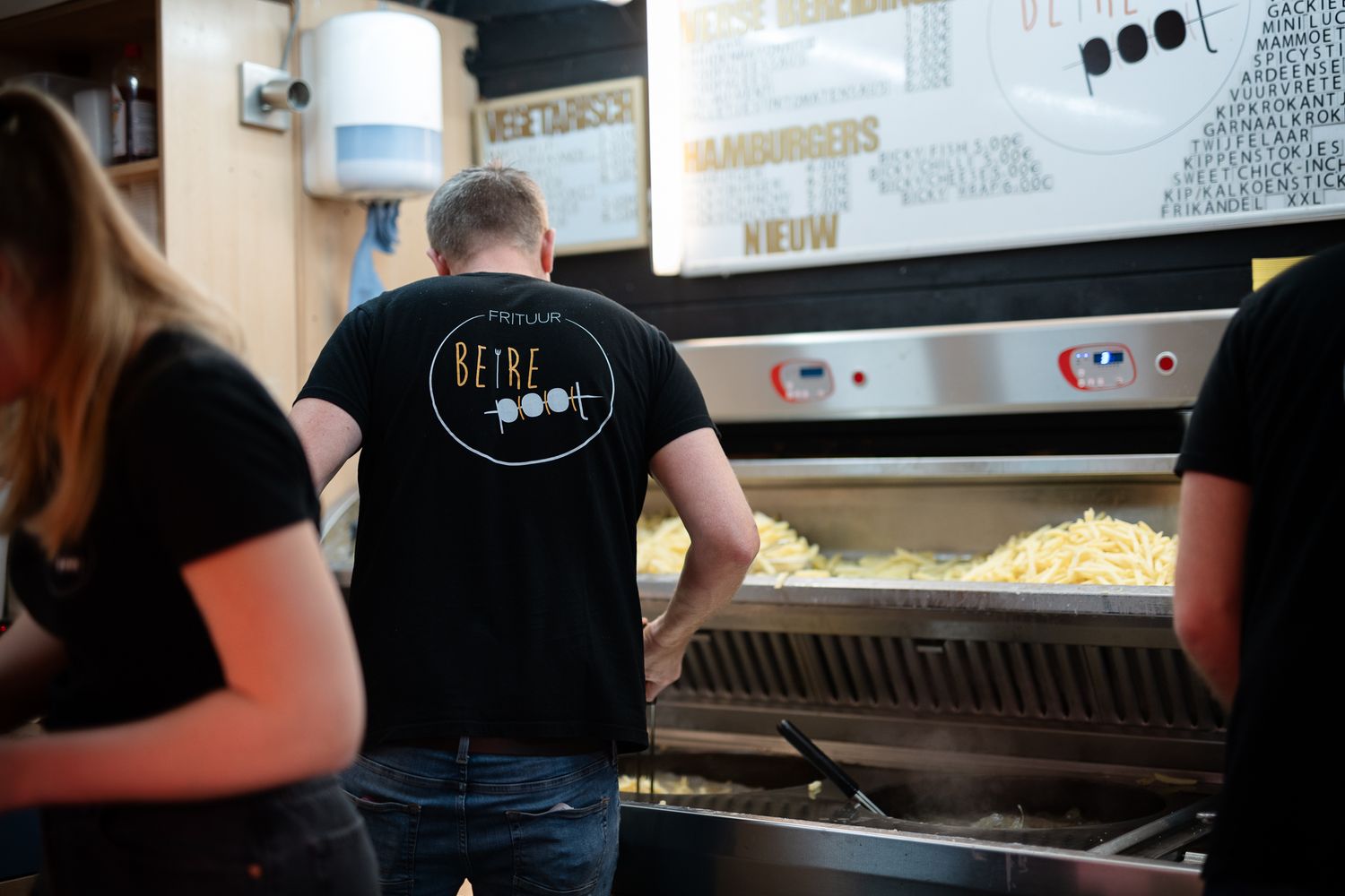 Staff in black Betre Poot shirts working at a commercial kitchen fry station.