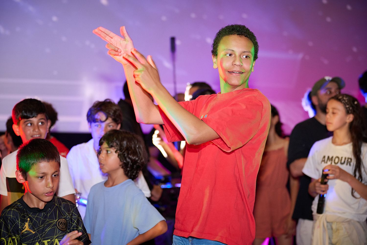 Children and adults dancing at a colorful indoor party event with purple and pink lighting.