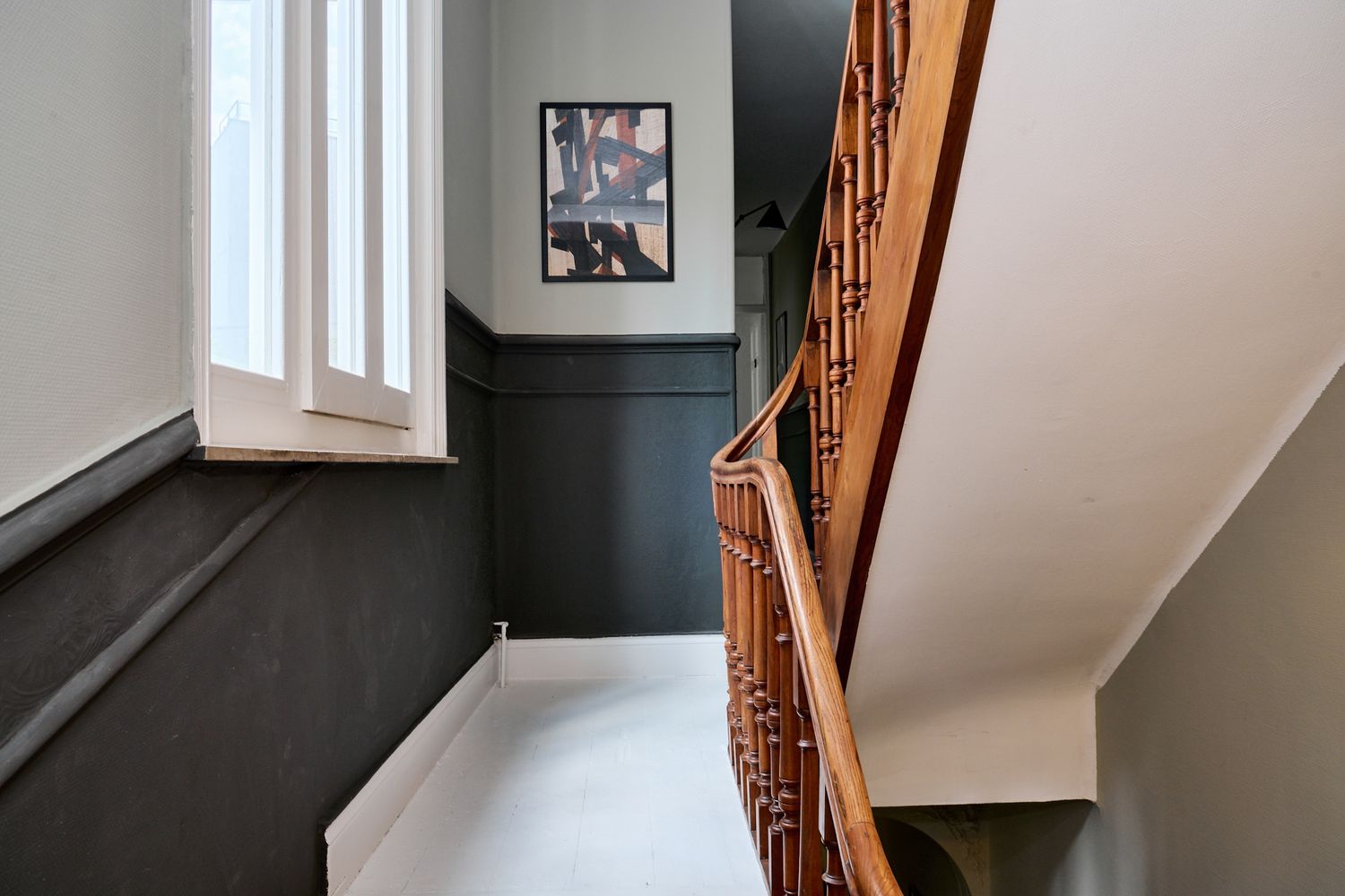 Elegant staircase with wooden banister, dark wainscoting, white walls, and framed artwork in a stylish home interior.
