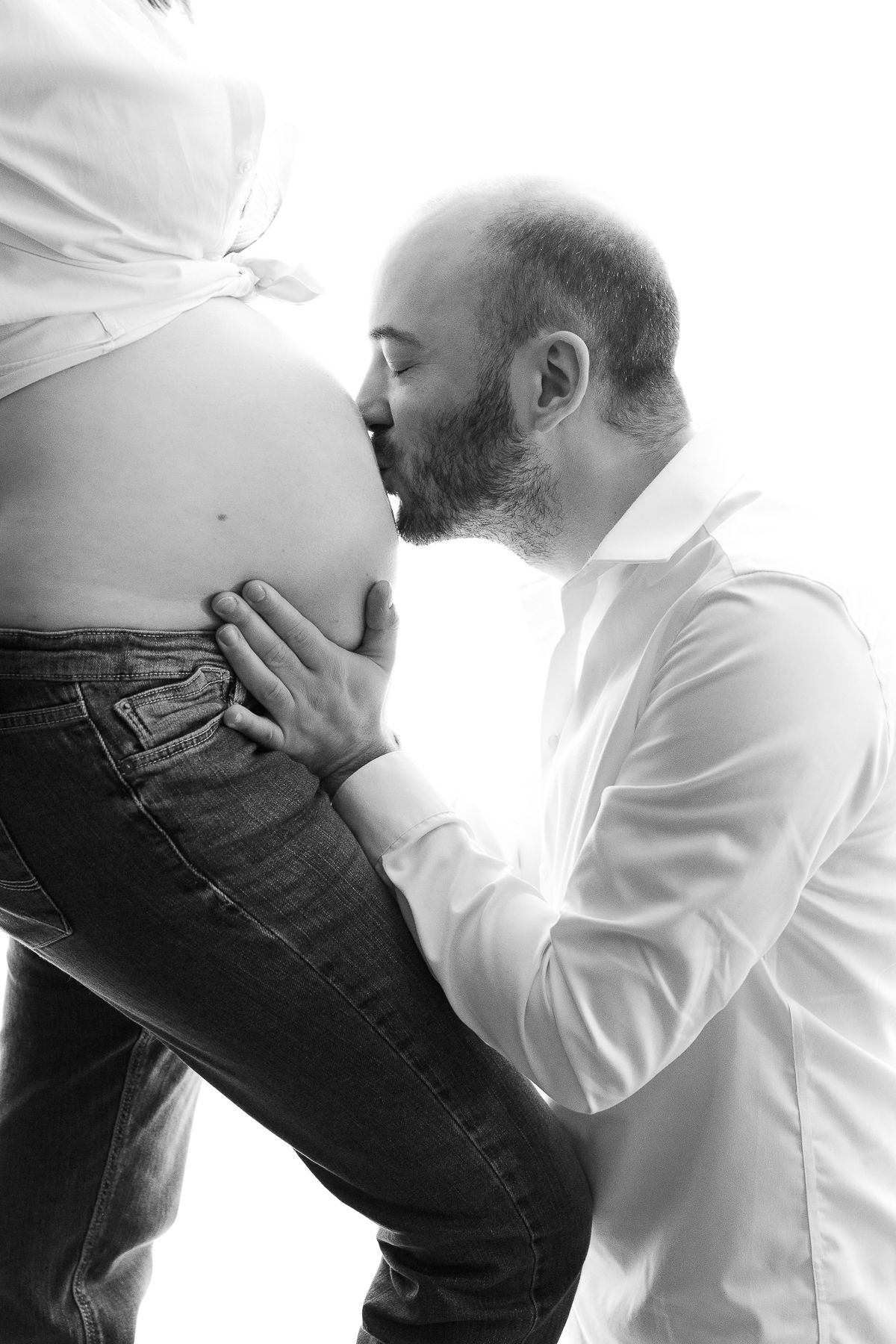 Black and white photo of a bearded man kissing a pregnant woman's belly, maternity photography concept.