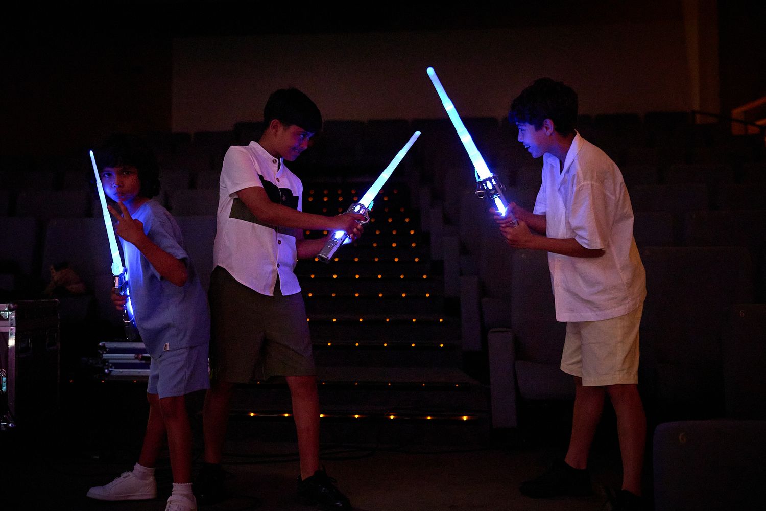 Children playing with glowing lightsabers in a dark room, recreating a Star Wars battle scene.