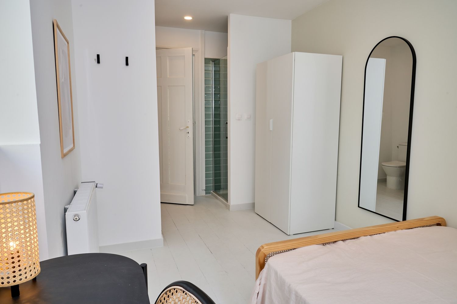 Minimalist studio room with white walls, arched mirror, wardrobe, and tiled bathroom entrance with modern decor.