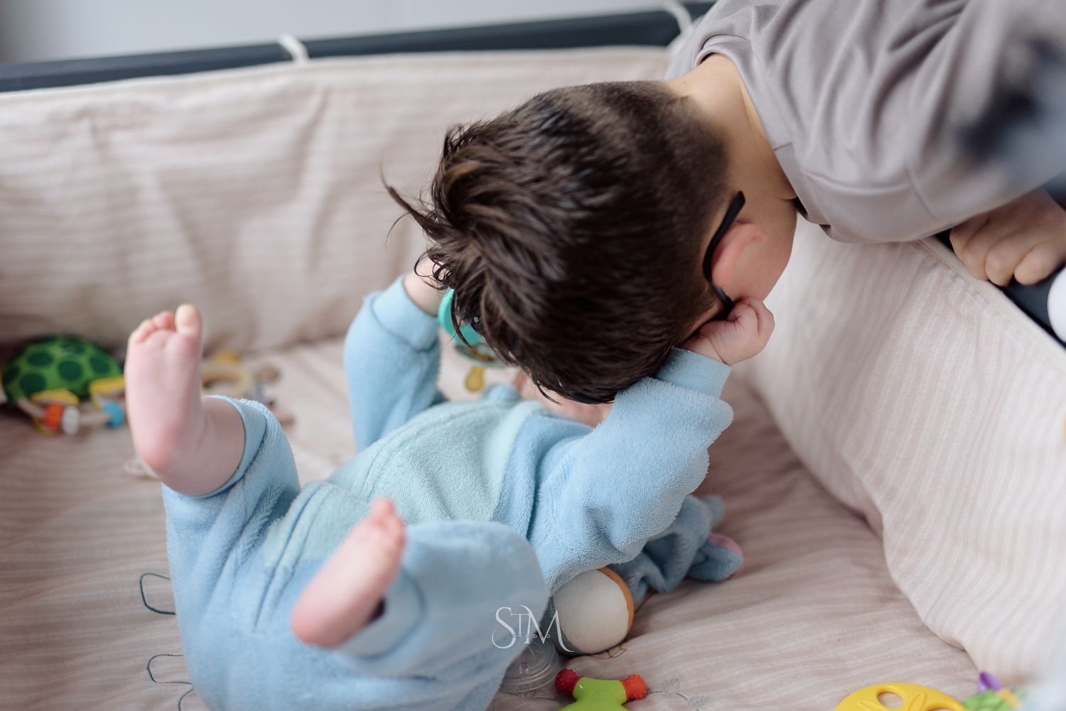 Overhead view of a baby in blue pajamas playing on a couch with colorful toys nearby.