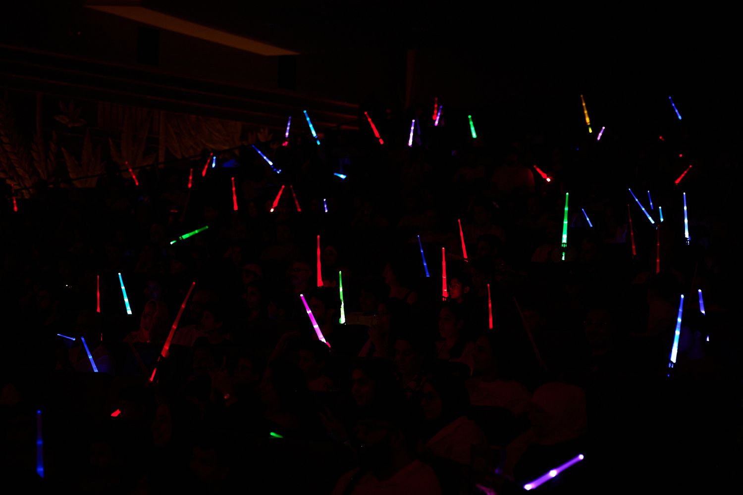 Crowd holding colorful glowing light sticks at a dark concert or party event.