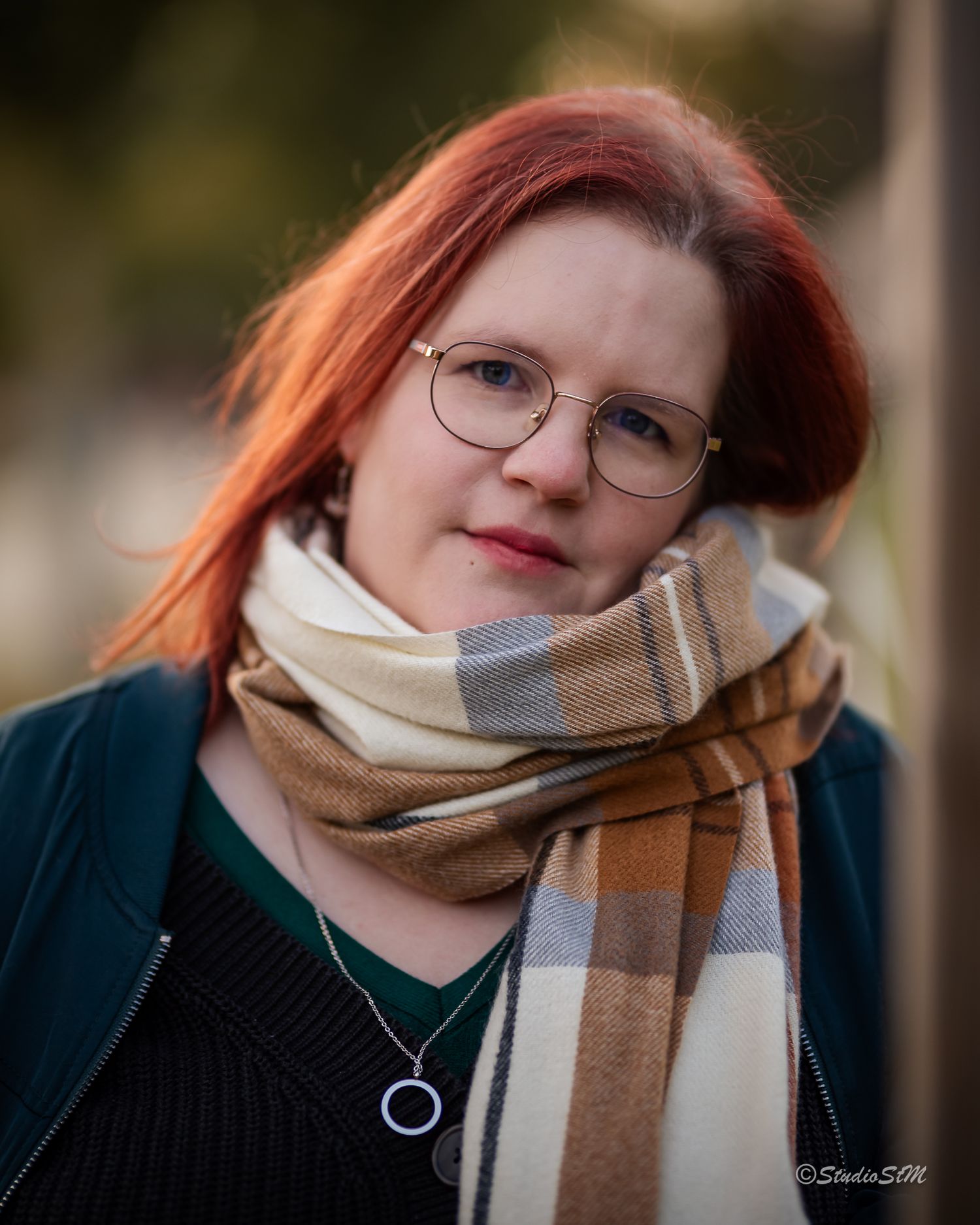 Close-up portrait of a red-haired woman in glasses wearing a plaid scarf outdoors.