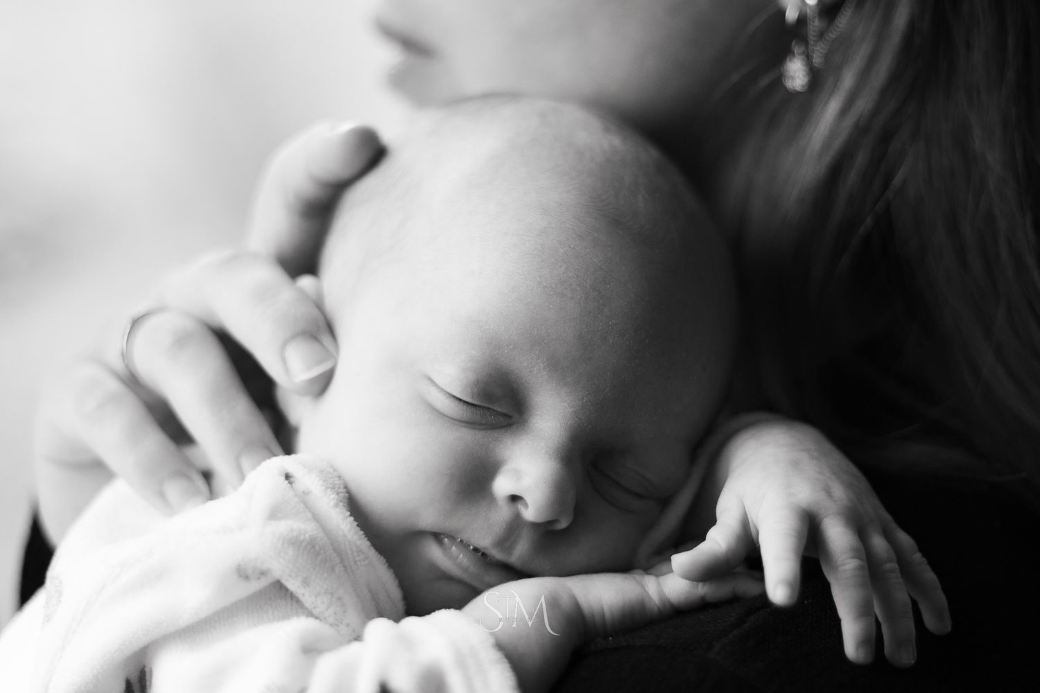 Black and white photo of a sleeping newborn baby cradled gently in a mothers arms.