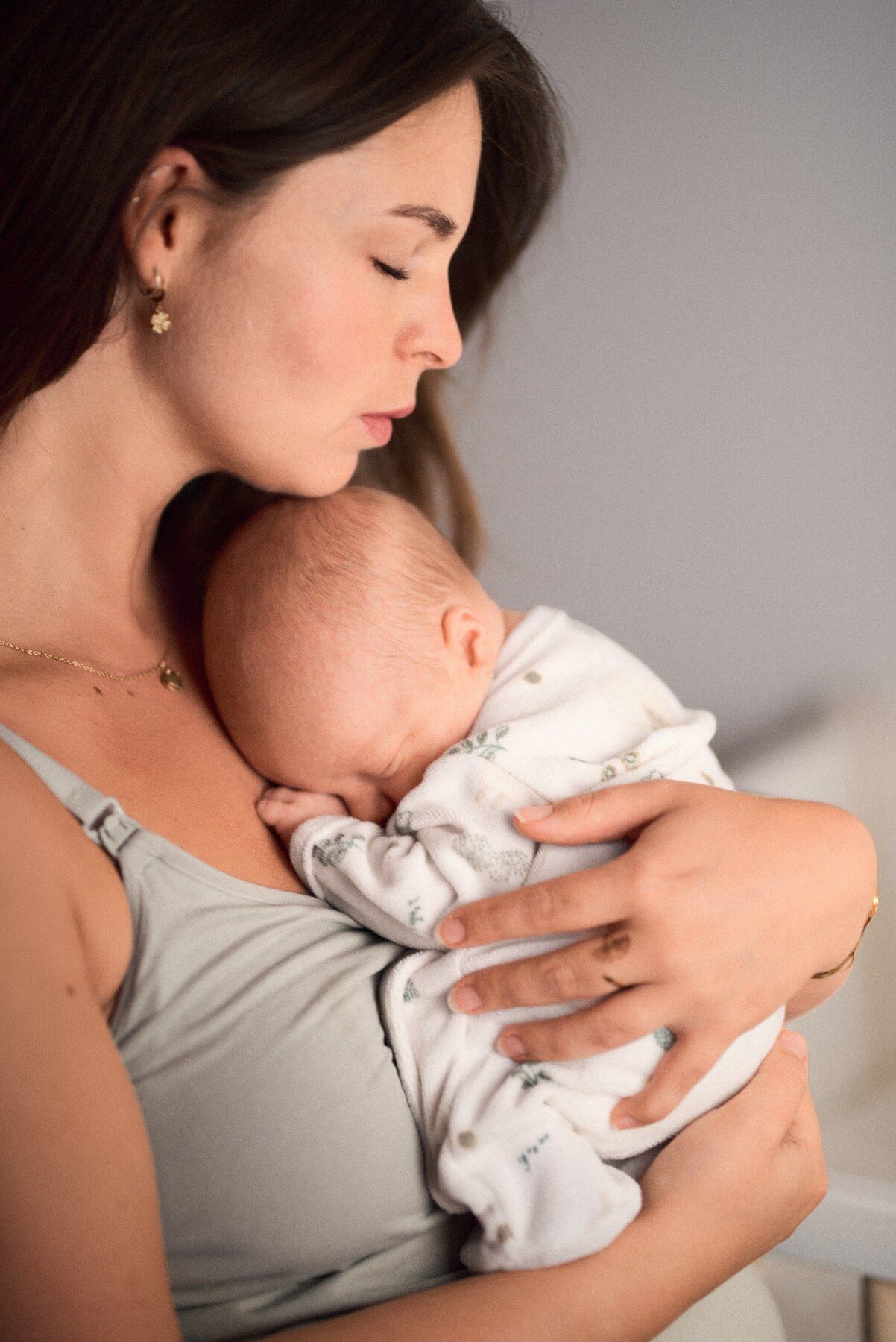 A mother tenderly kisses her sleeping newborn baby held close to her chest.