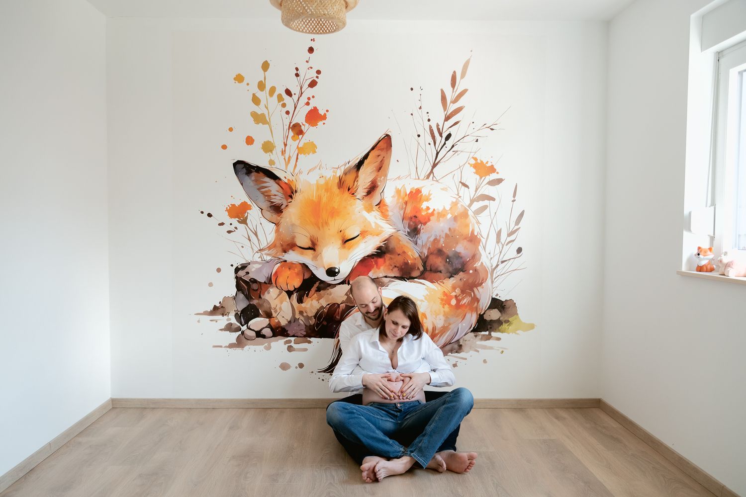 A woman sits beneath a large watercolor fox mural in a bright, minimalist room with wood floors and a window.
