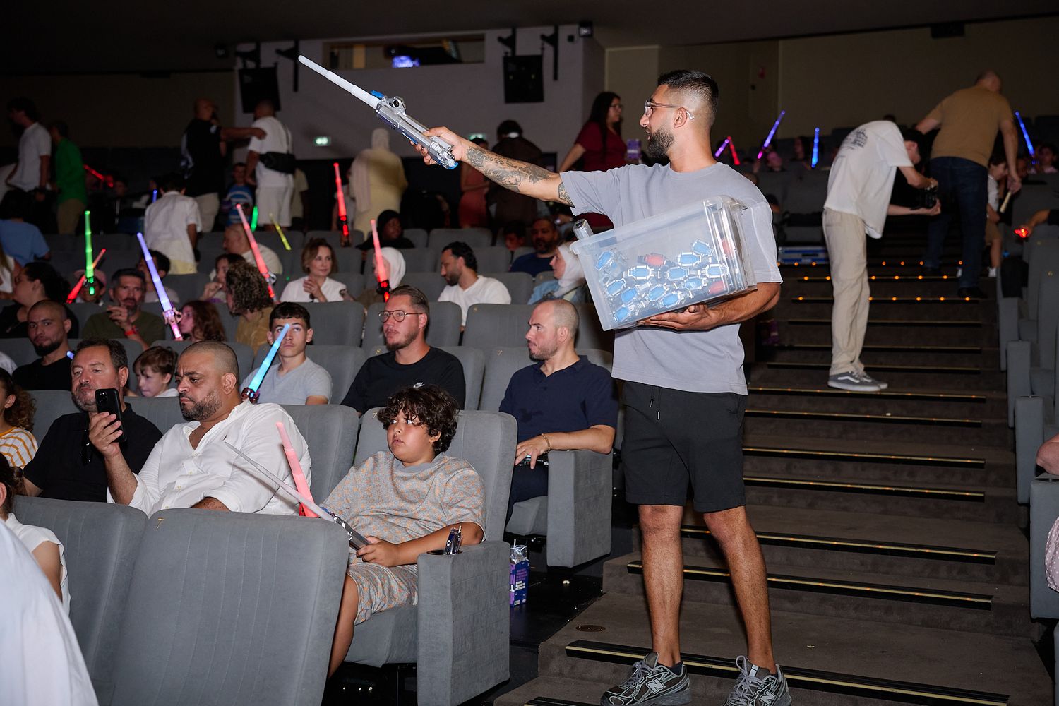 Man wielding a lightsaber at a Star Wars themed movie screening with audience holding glowing sabers.