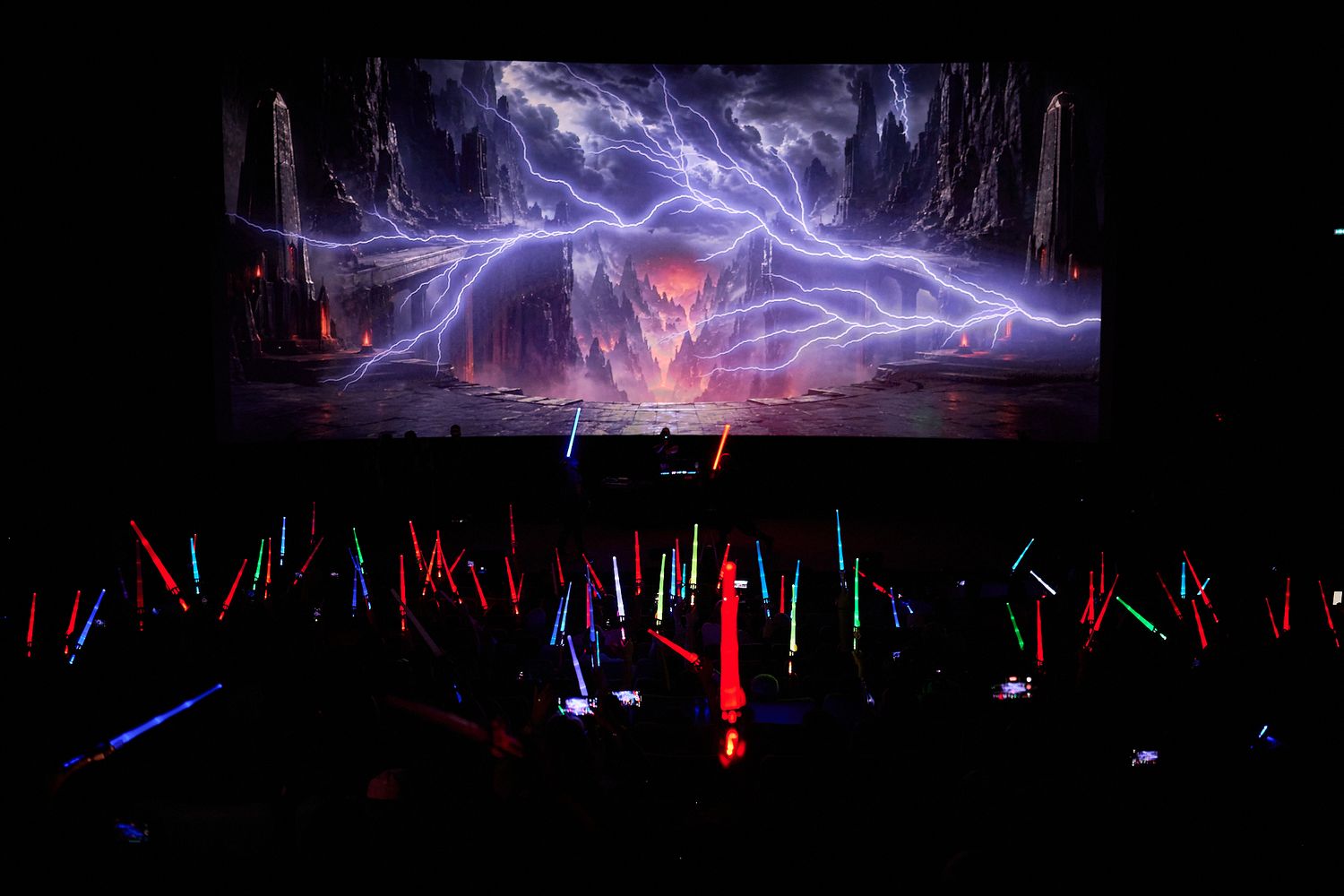 Star Wars concert with colorful lightsabers audience and dramatic lightning battle scene projected on stage screen.