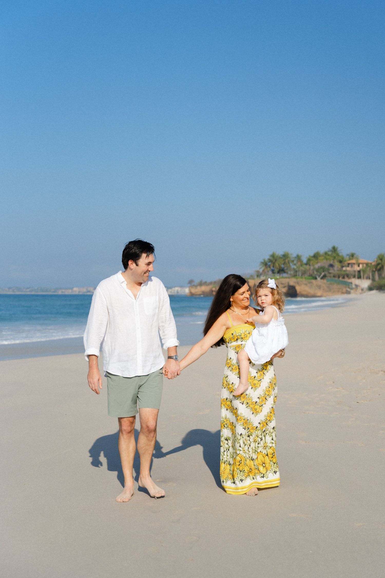 Mom holding baby and walking hand in hand with husband on the beach at Four Seasons Punta Mita Mexico — Marina Pochepkina Photography