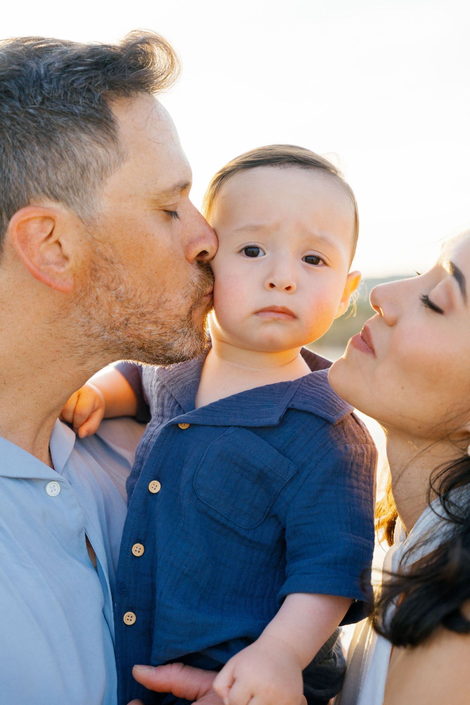Mom and dad kissing their toddler who are looking to camera in Punta Mita - Marina Pochepkina photography