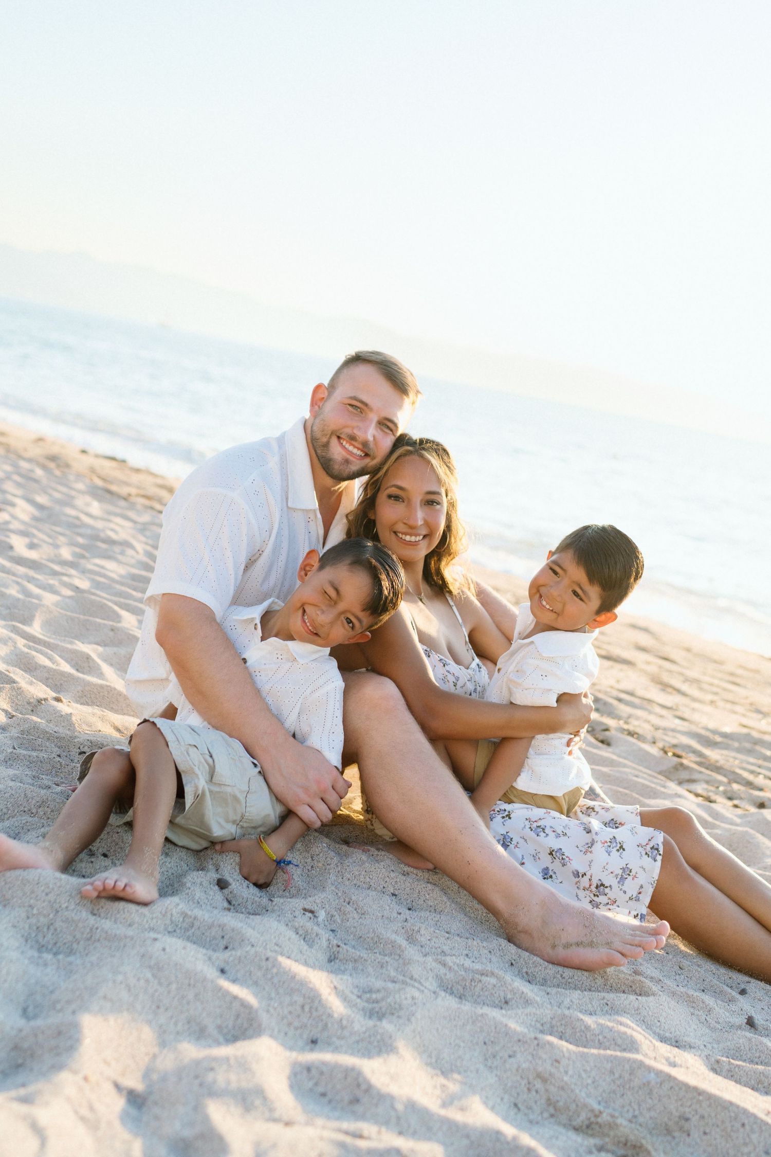 Family of four sitting on the sand and smiling at the camera during golden hour beach session in Puerto Vallarta Mexico — Marina Pochepkina