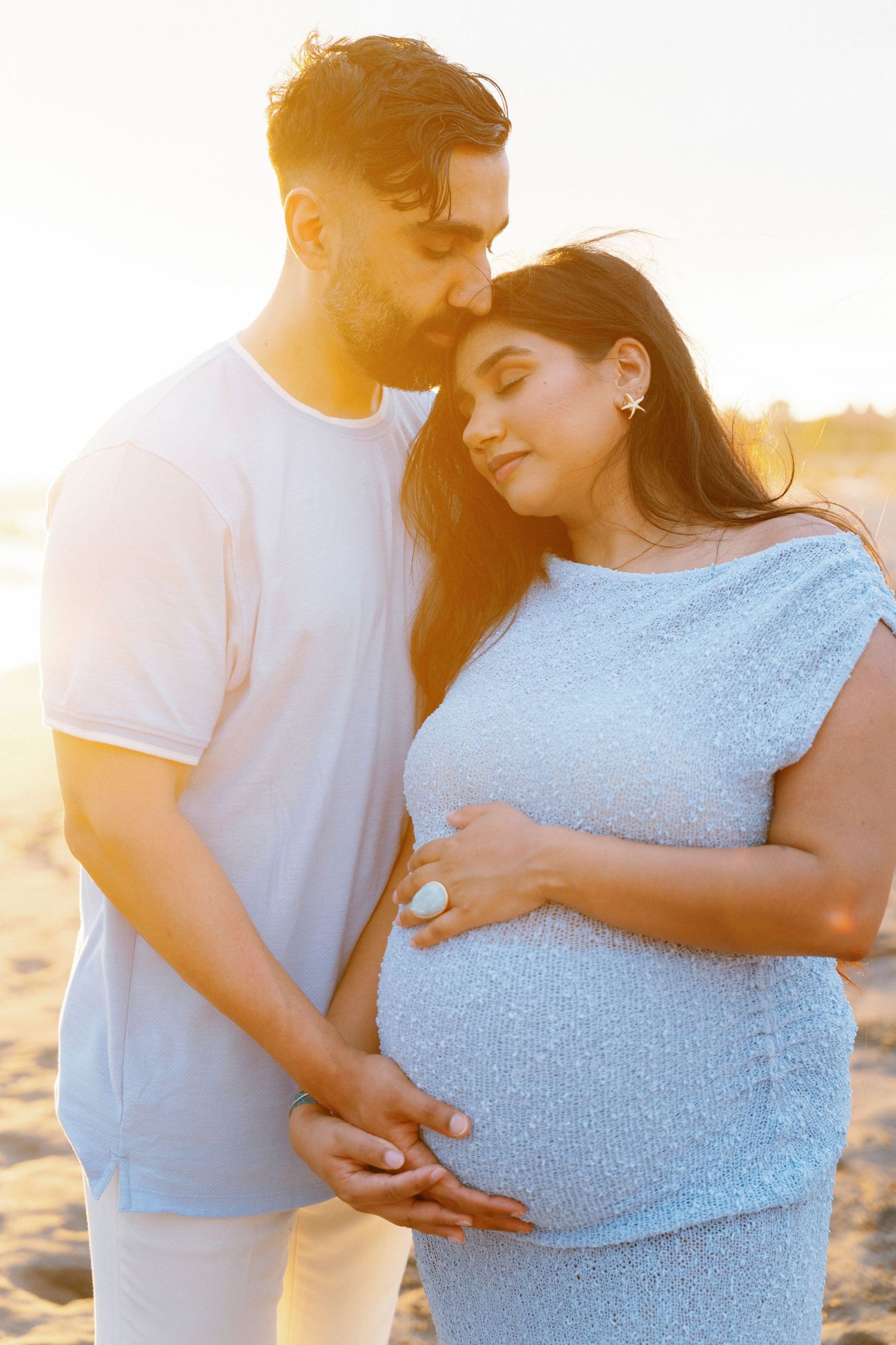 A couple embraces on a beach at sunset, with the pregnant woman cradling her baby bump Vidanta hotel -Marina Pochepkina photography