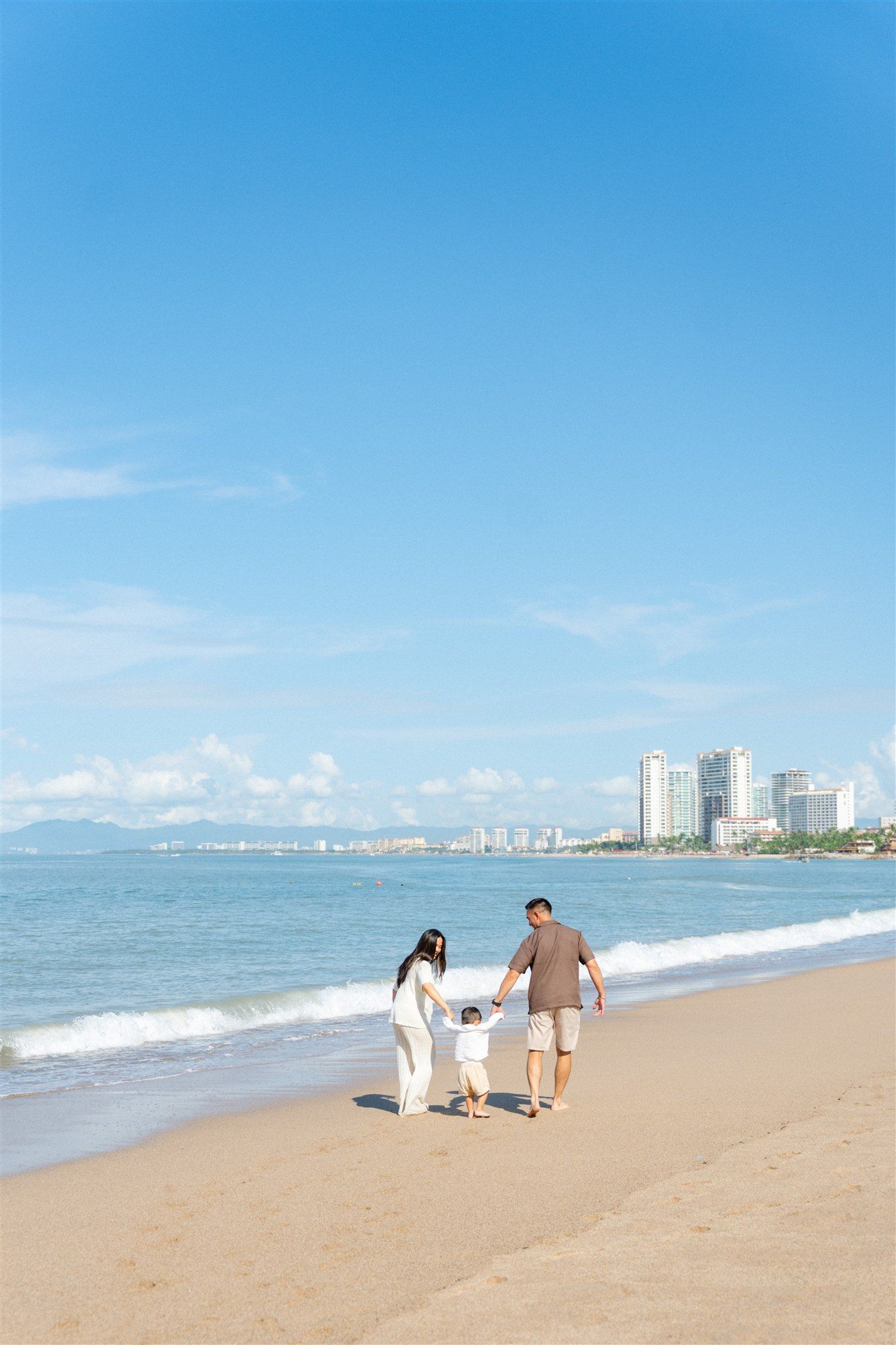 Mom and dad walking away from camera hand in hand with toddler on the beach in Nuevo Vallarta Mexico — Marina Pochepkina Photography