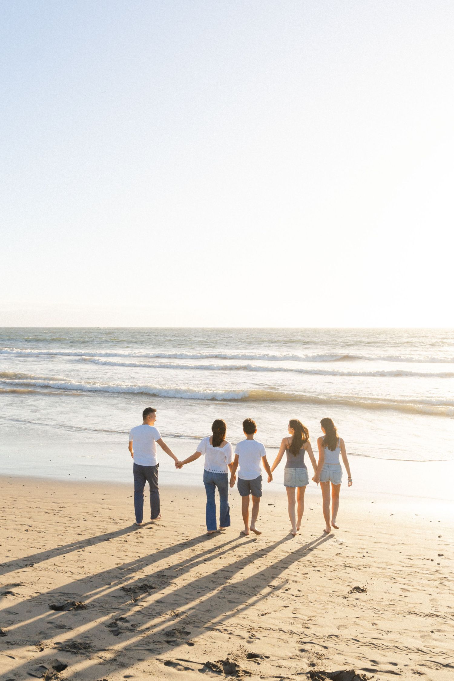 Five people big family holding hands walking toward ocean waves on a sunny sandy beach in Puerto Vallarta - Marina Pochepkina photography