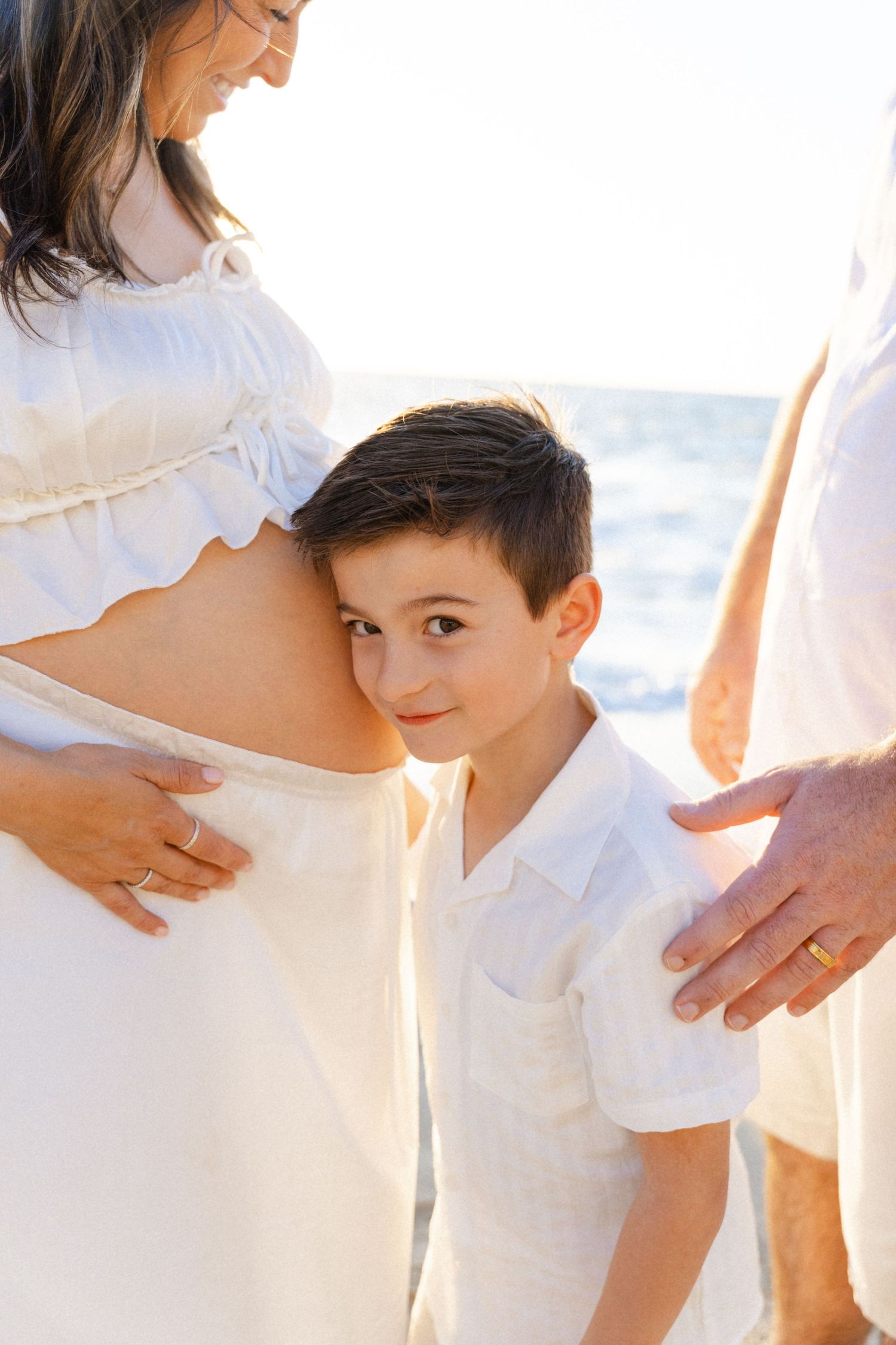 A little boy rests his head on his pregnant mother's belly at the beach, surrounded by family in Four Seasons Punta Mita -Marina Pochepkina