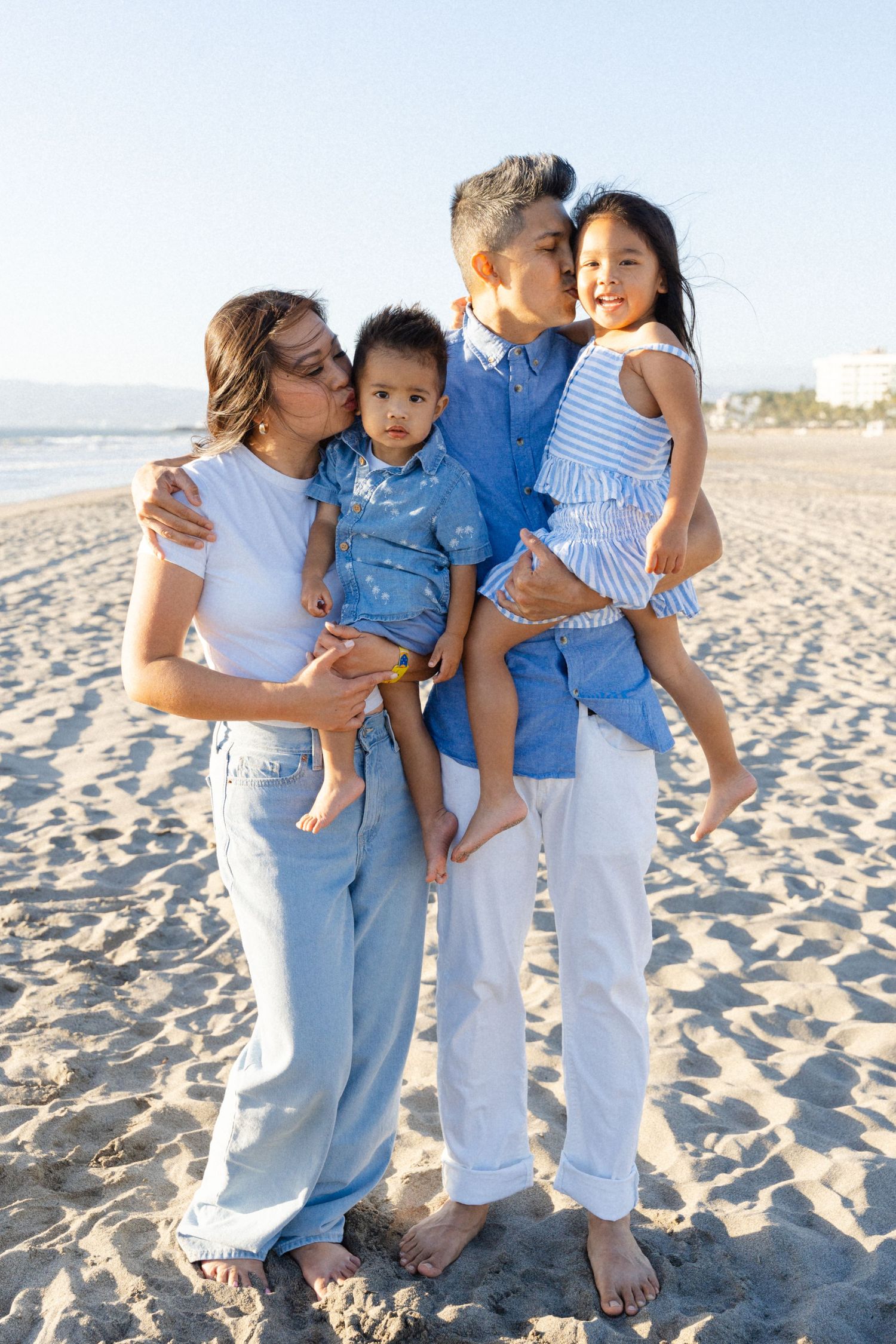 Mom and dad simultaneously kissing their kids during a family session on the beach in Puerto Vallarta Mexico — Marina Pochepkina Photography
