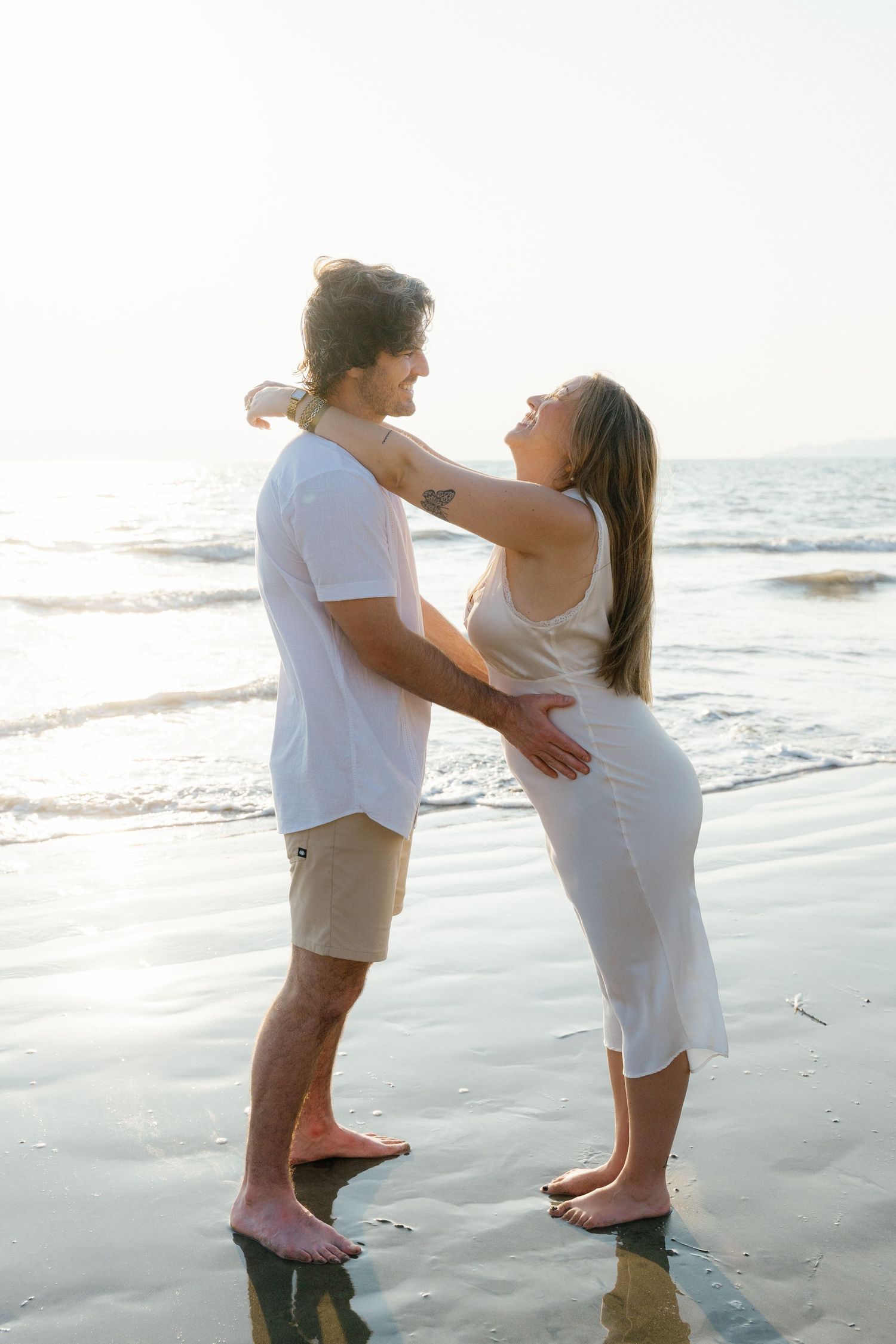 Couple embracing barefoot on a sunny beach, woman in white dress laughing in Puerto Vallarta — Marina Pochepkina photography