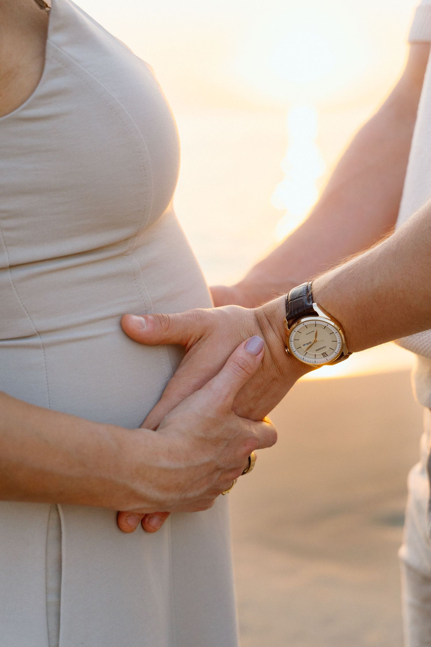 Pregnant woman  with partner's hands on baby bump at sunset beach in Mariott hotel Puerto Vallarta-  Marina Pochepkina photography