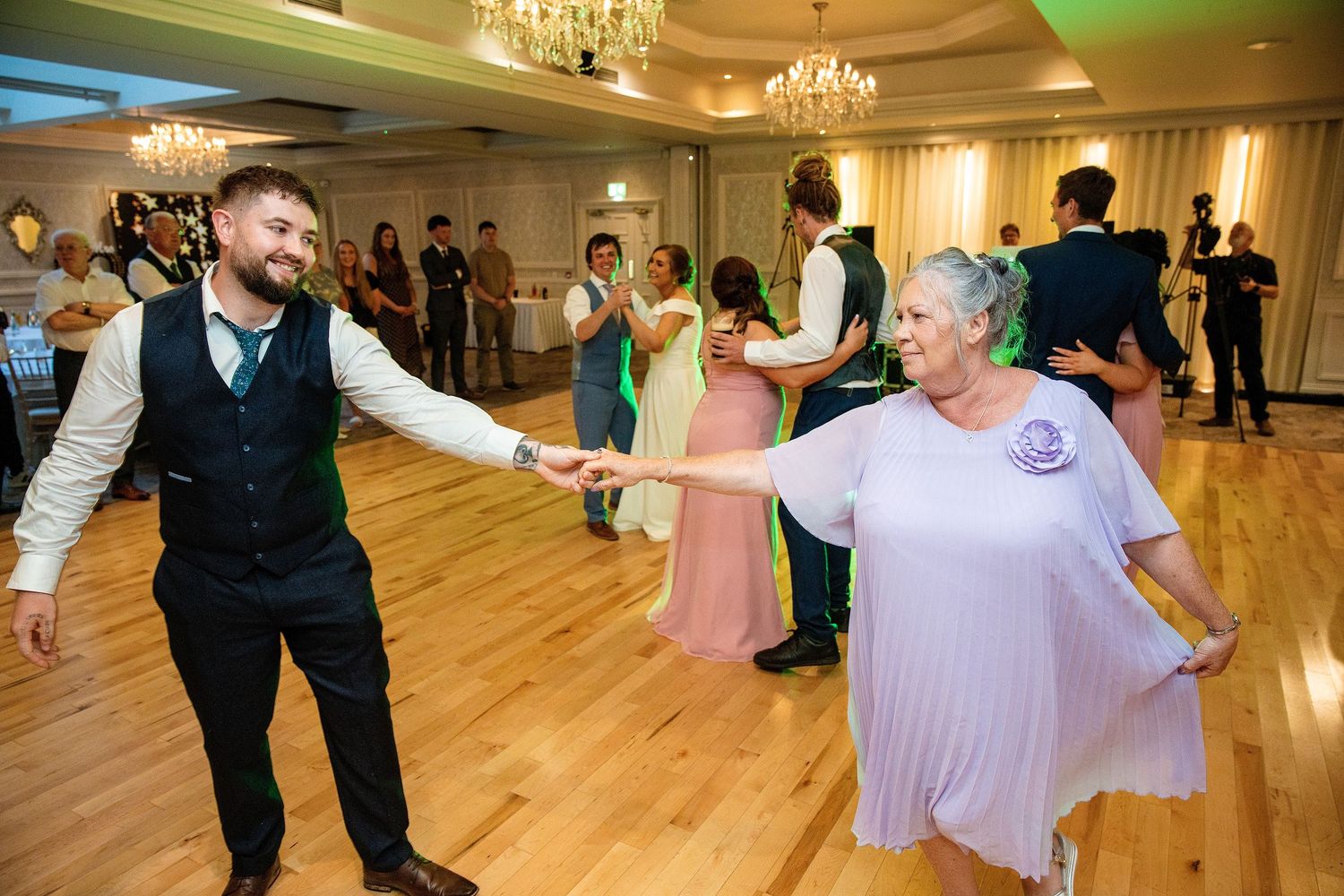 Joyful couple dancing together at a wedding reception on a wooden dance floor in an elegant ballroom.