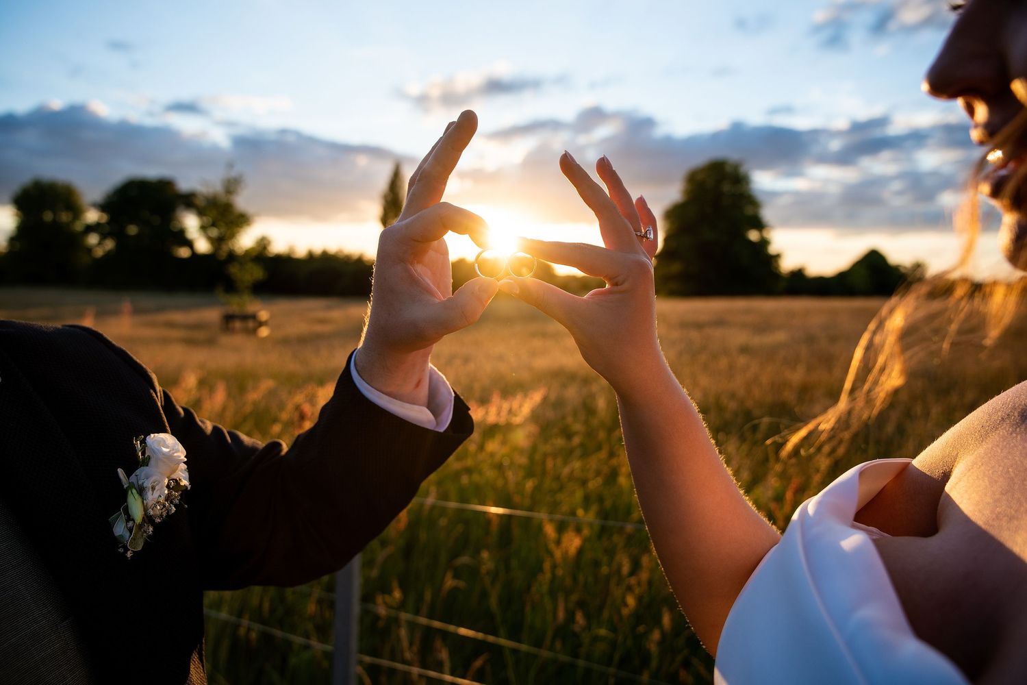 Couple framing the golden sunset between their hands in a romantic field during magic hour.