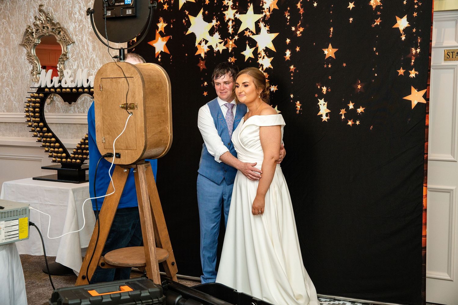 Bride and groom posing together in front of a star-decorated black backdrop at their elegant wedding reception.