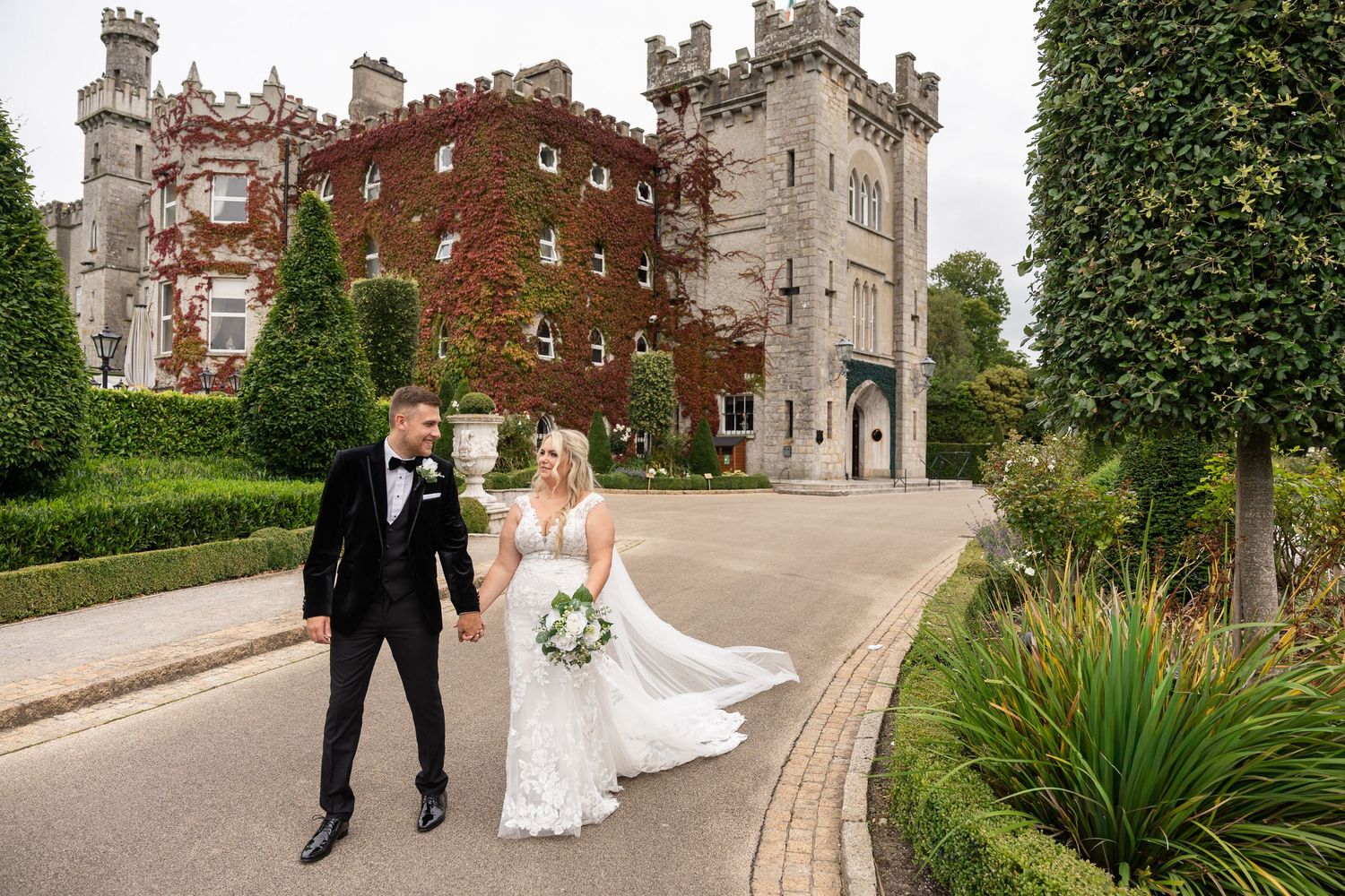 A couple celebrates their wedding day in front of a majestic Irish castle with ivy-covered stone walls and towers.