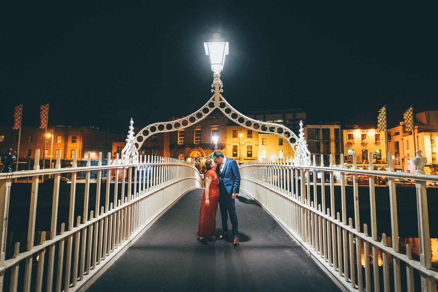 Couple sharing a romantic moment on the illuminated Ha'penny Bridge in Dublin at night.
