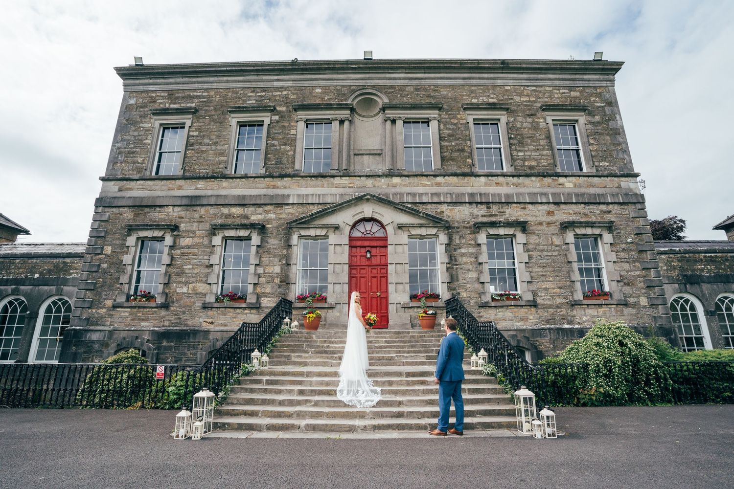 Bride and groom stand on stone steps of elegant historic wedding venue with red door in Ireland at Bellinter house.
