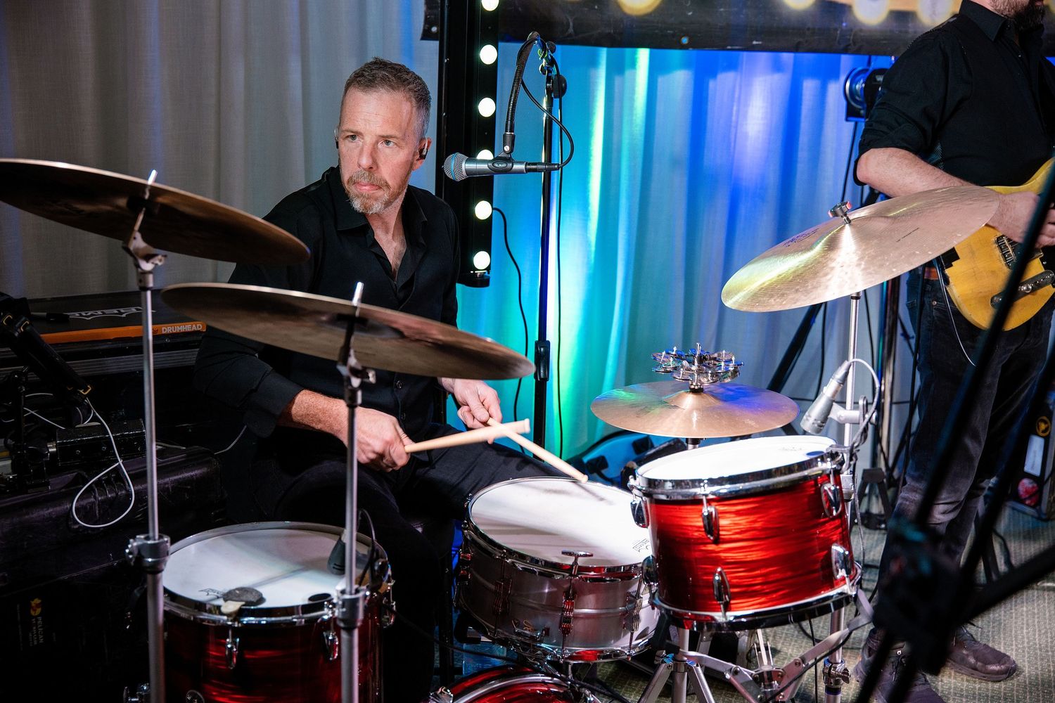 Professional drummer performing live on stage with cymbals and red drum kit under blue stage lights.